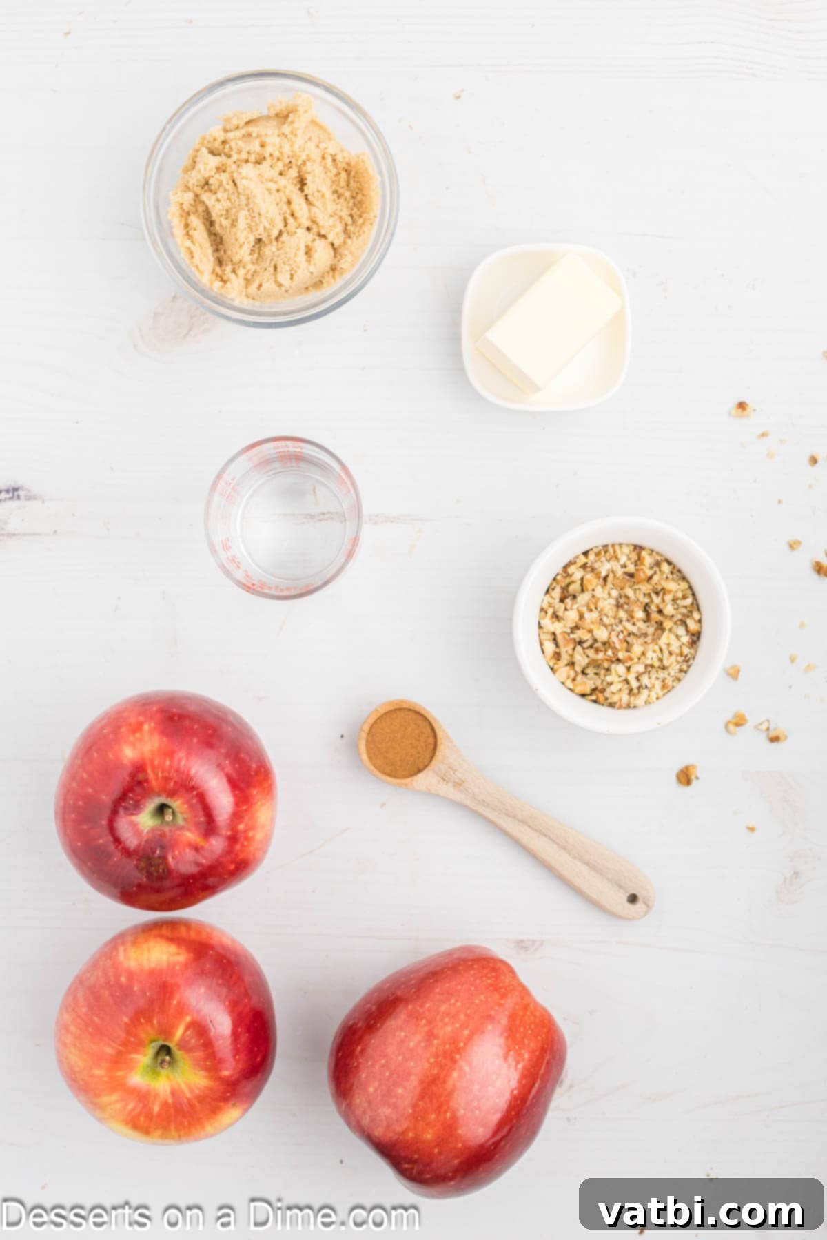 Warm Spiced Baked Apples 2 A flat lay photograph showcasing all the fresh ingredients needed for baked apples: vibrant red apples, a bowl of rich brown sugar, ground cinnamon in a small dish, softened butter, and a pile of finely chopped walnuts.