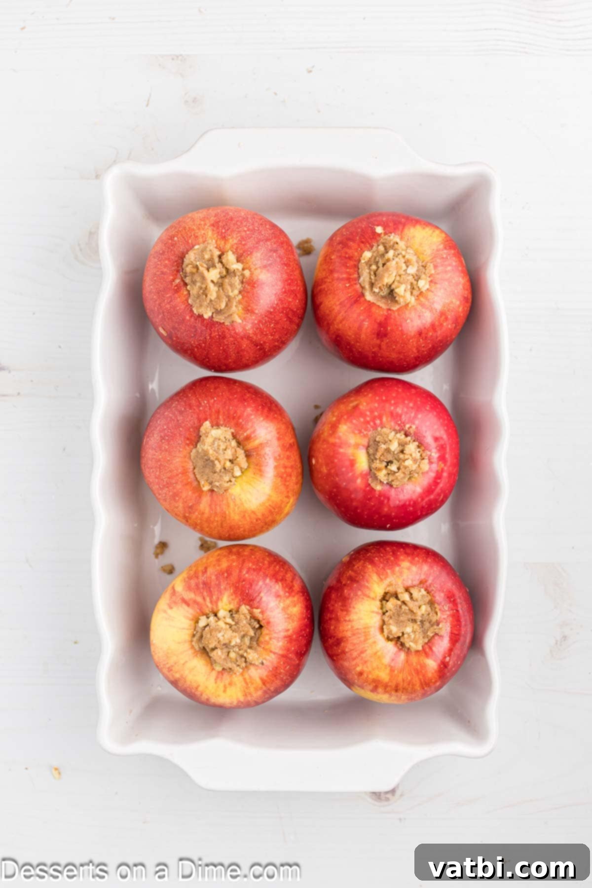 Warm Spiced Baked Apples 5 Cored apples in a baking dish, each generously filled with the brown sugar, cinnamon, butter, and walnut mixture, with water poured at the bottom of the pan, ready for baking.