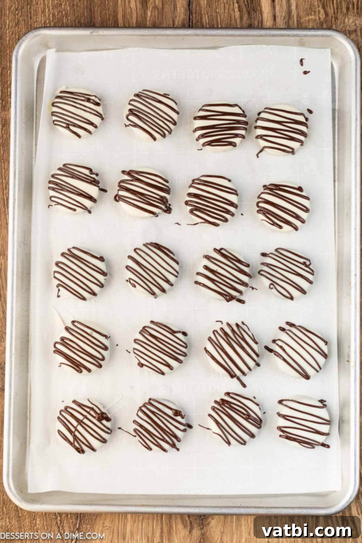 Decadent White Chocolate Oreos 5 White chocolate covered Oreos with a contrasting chocolate drizzle on a baking sheet, ready for final setting.