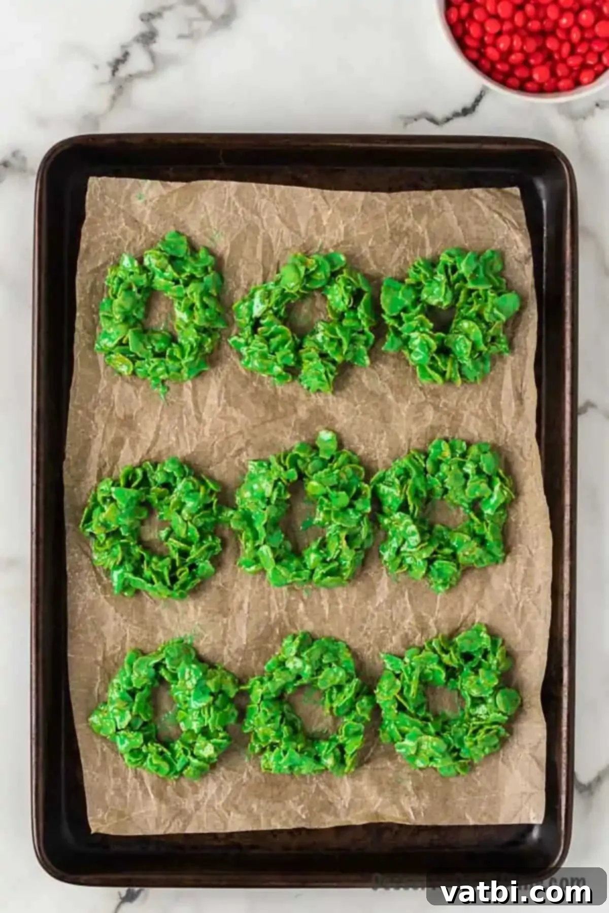 Sweet Christmas Wreath Delights 7 Wreath shapes made from cornflake mixture arranged on a baking sheet lined with parchment paper.