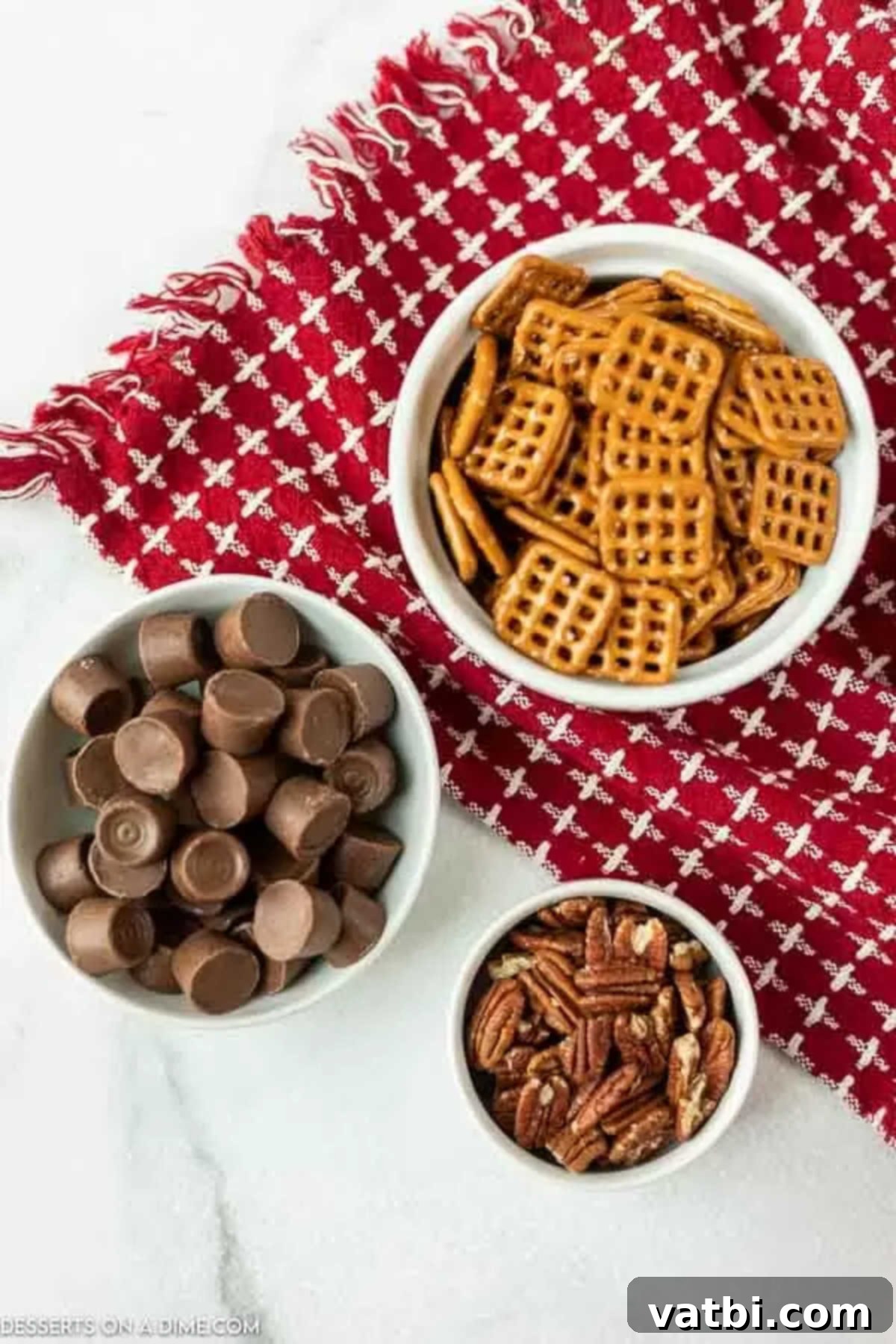 Ingredients for Rolo Pretzel Turtles recipe: a bowl of square pretzels, unwrapped Rolo candies, and pecan halves.