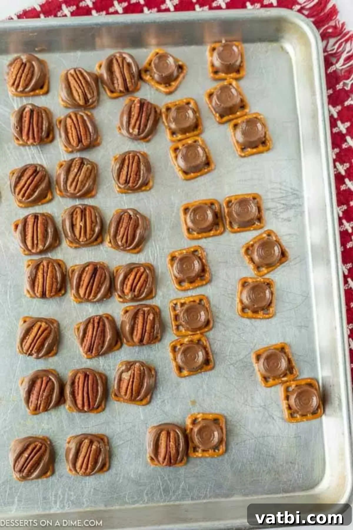 A hand gently pressing a pecan half onto a melted Rolo candy on a pretzel, demonstrating the final step before cooling.