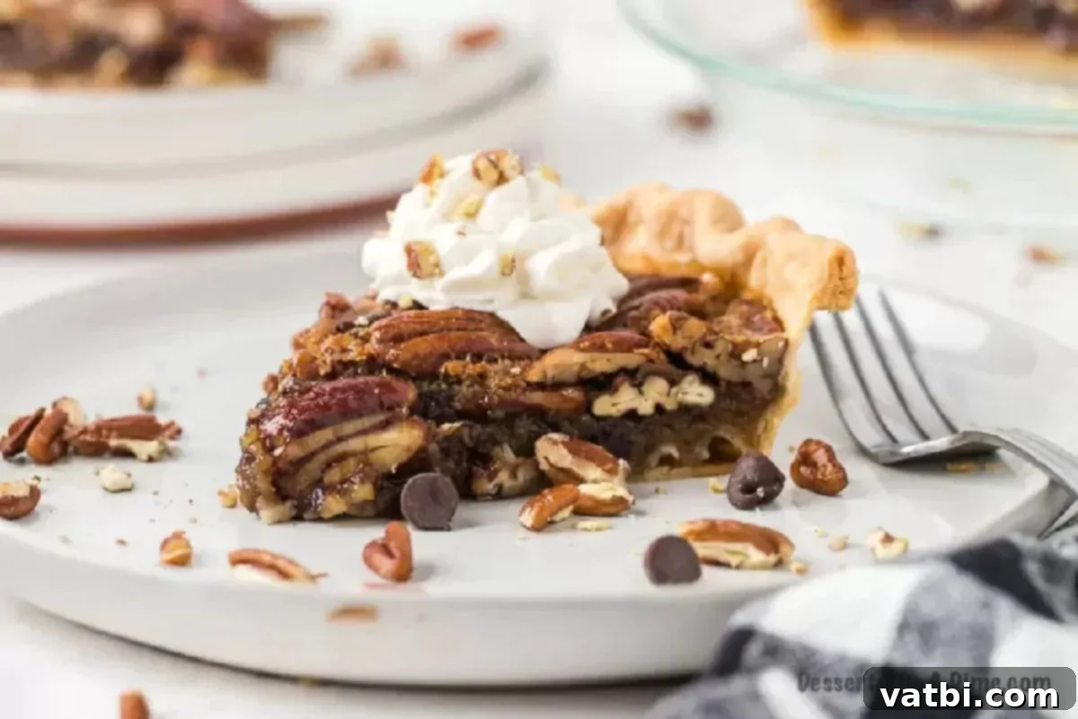 Slice of chocolate pecan pie on a plate with whipped cream, ready to be served as a decadent holiday dessert. 
