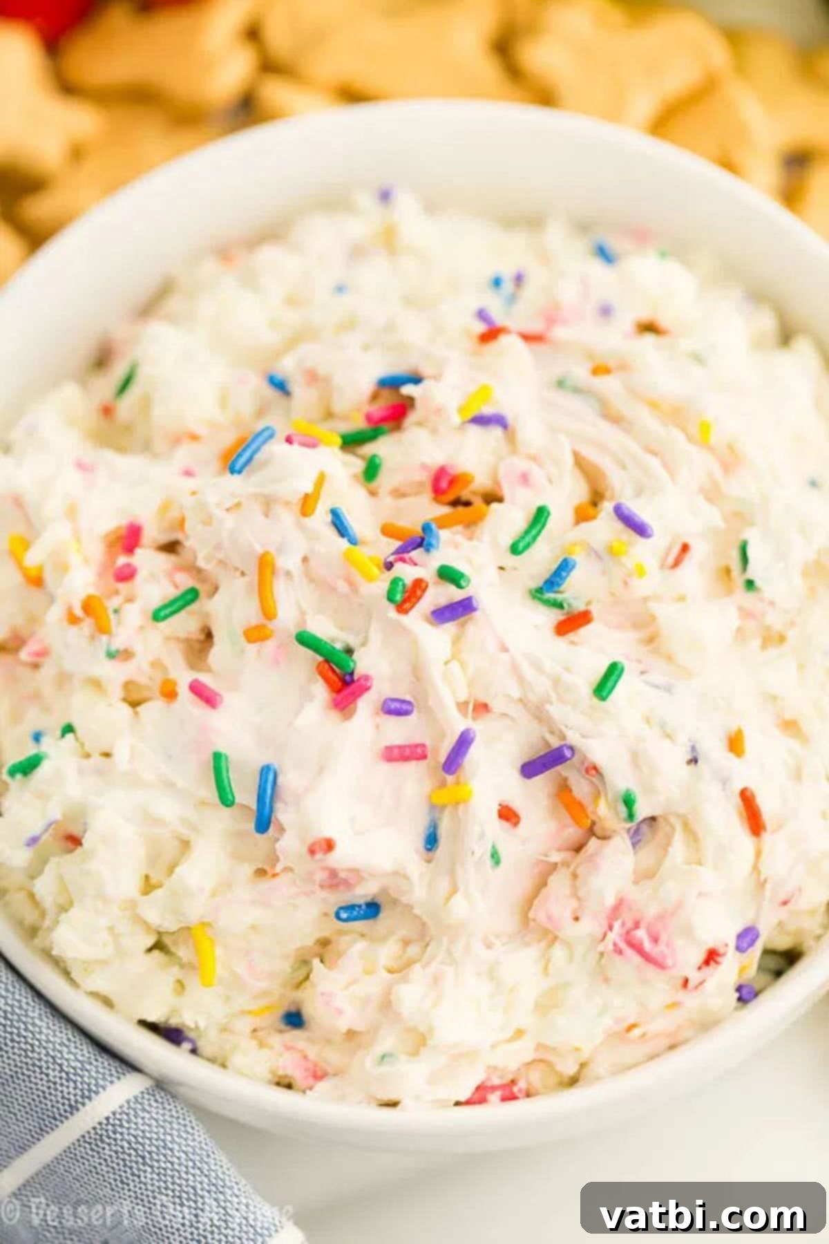 You only need 4 ingredients to make this decadent Cake Batter Dip Recipe. Serve it with fruit, graham crackers or anything you like for an amazing treat. A close-up shot of the creamy Cake Batter Dip, with a spoon taking a scoop, showcasing its smooth texture and colorful sprinkles.