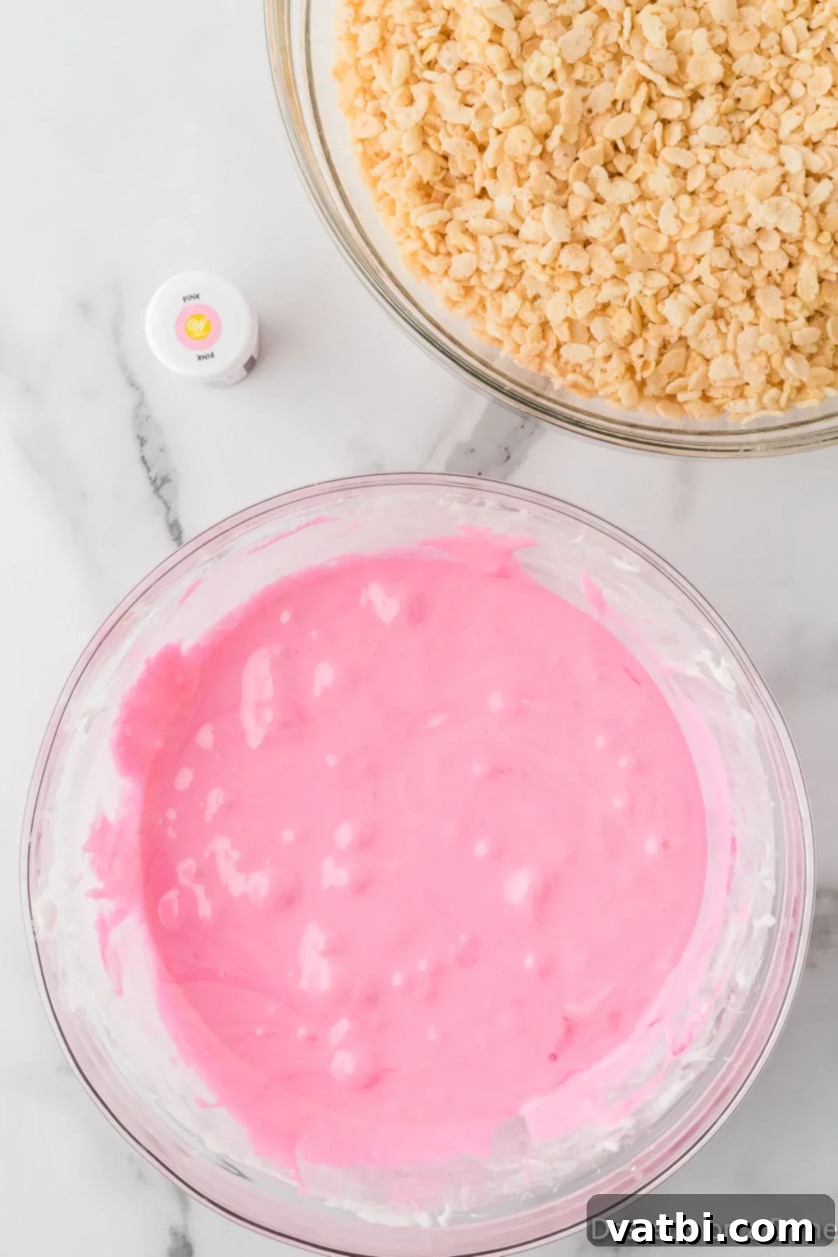 Pink food coloring added to the melted marshmallow and butter mixture, being stirred for even color distribution.