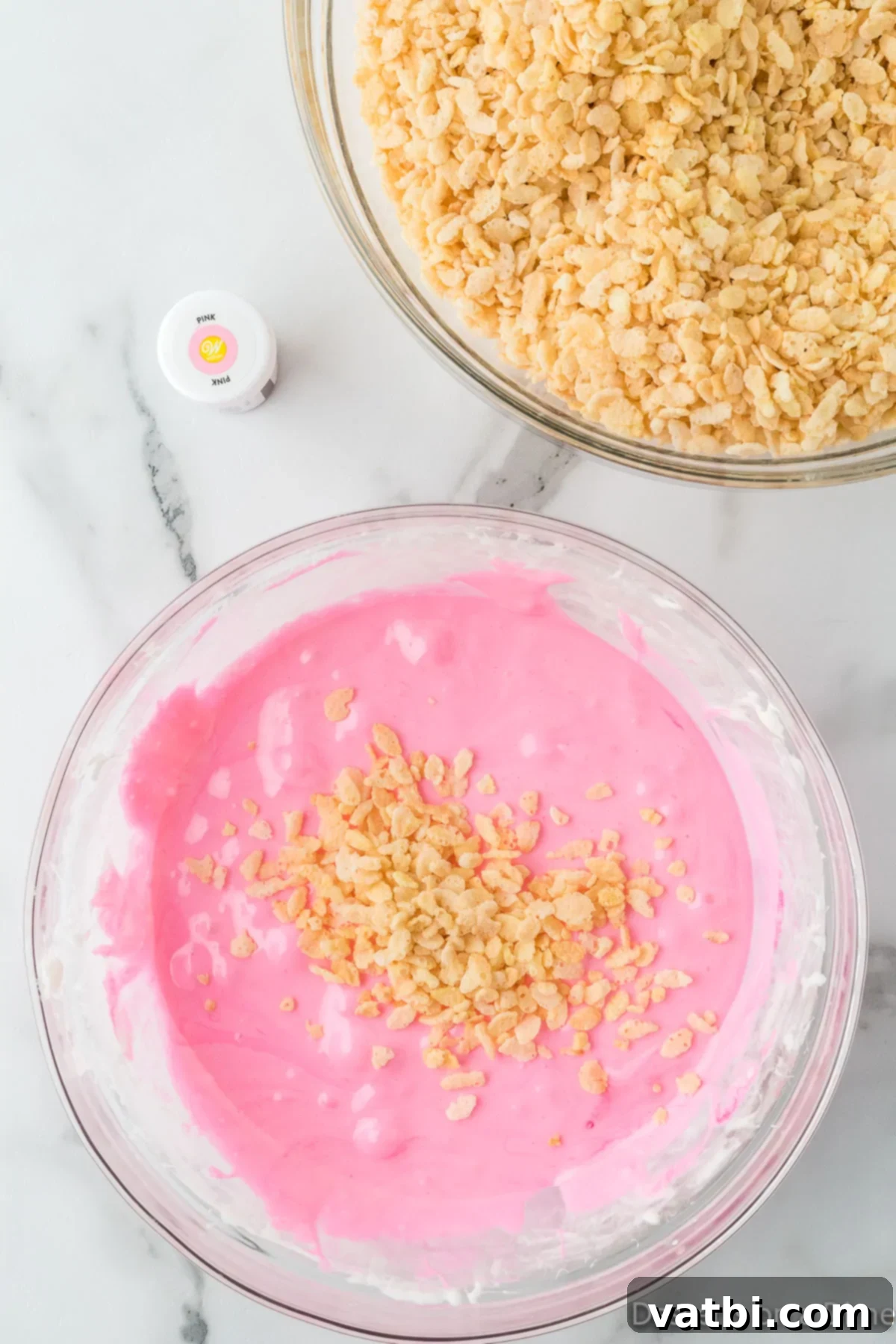 Rice Krispie cereal being added to the pink marshmallow mixture, ready to be coated.