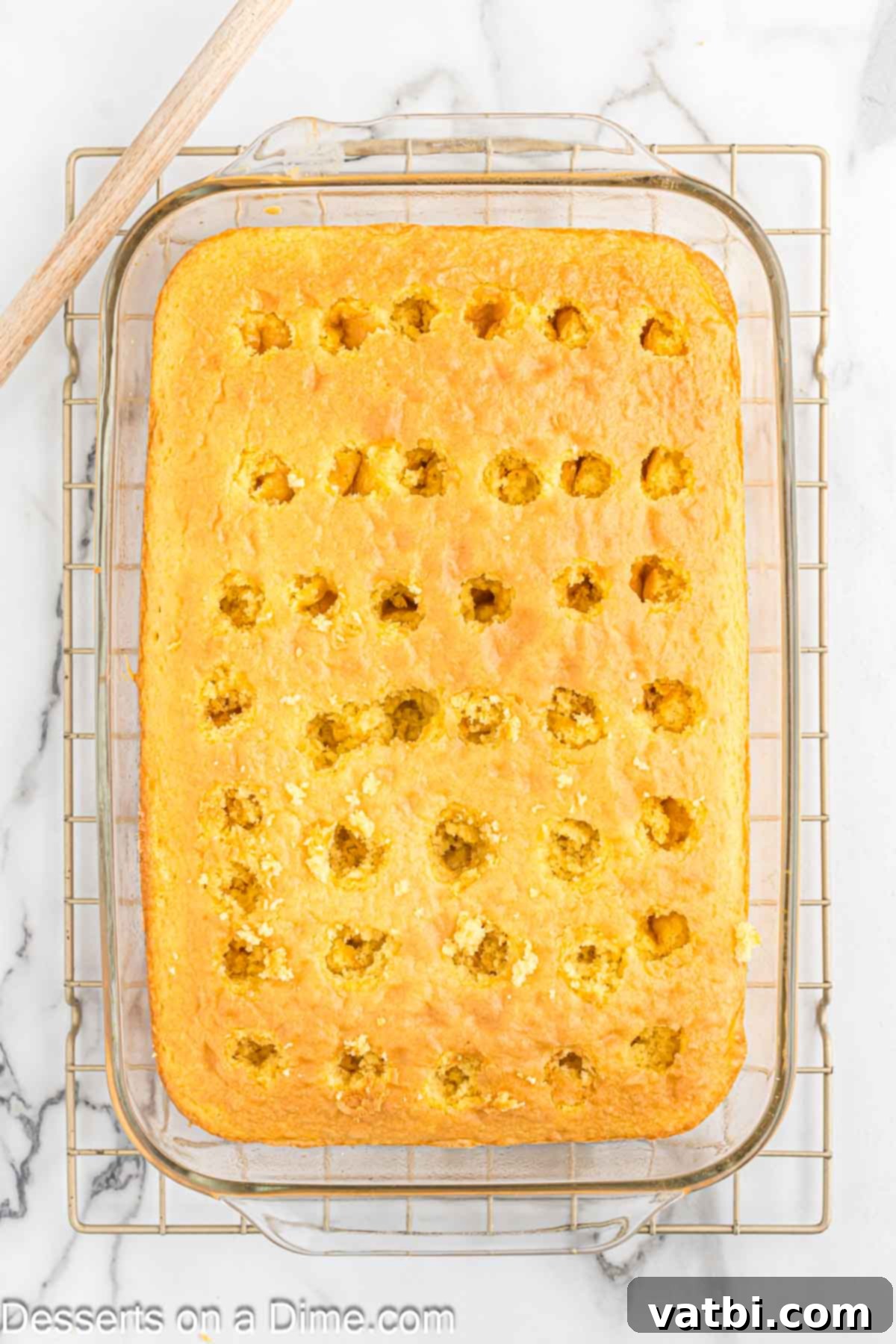 Tangy Lemon Infusion Cake 5 A close-up of the warm lemon cake being poked with the handle of a wooden spoon to create holes for the jello mixture.