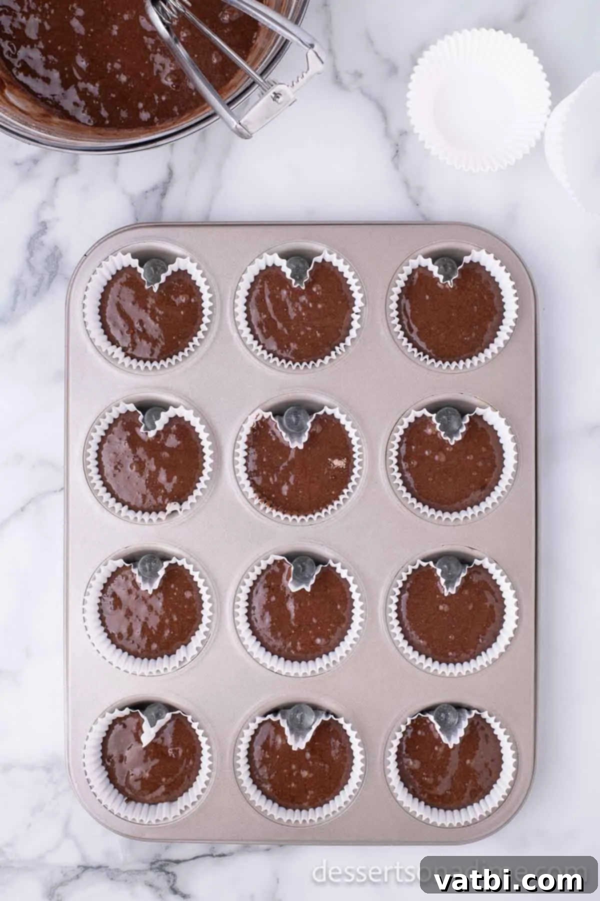 Cupcake batter poured into heart-shaped liners in a muffin pan, ready for baking.