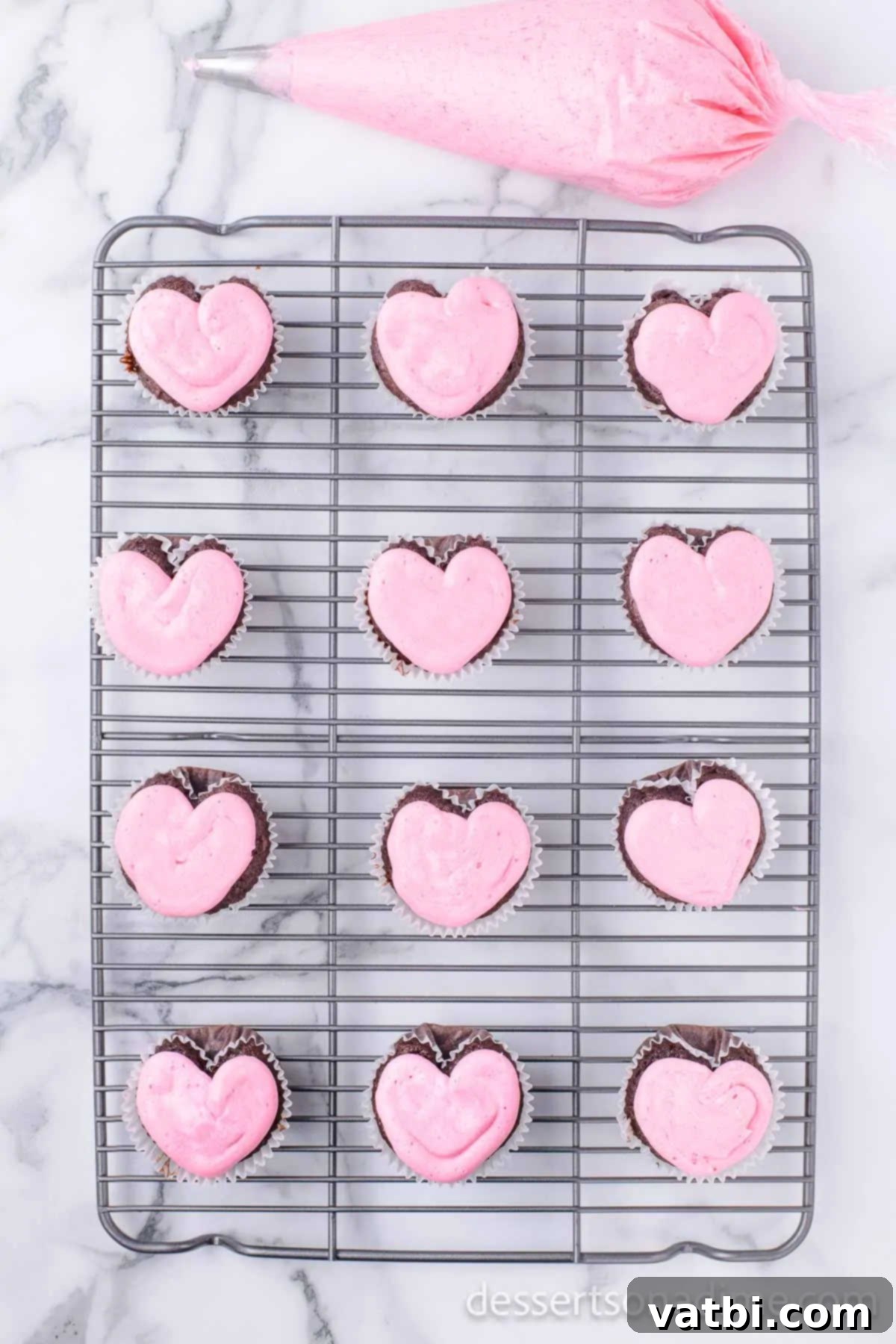 Pink icing piped onto the top of cooled heart-shaped cupcakes.