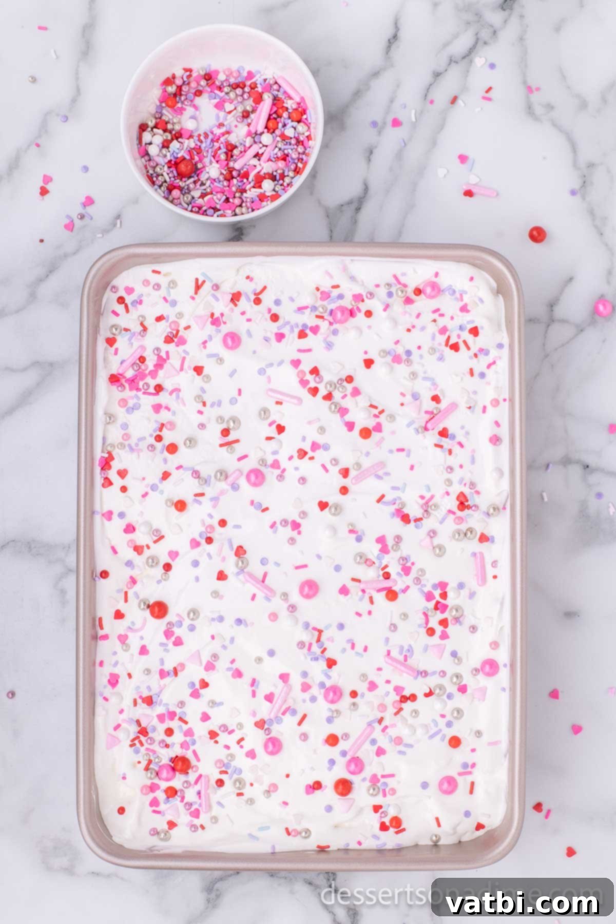 Sweet Valentine's Poke Cake 7 Whipped topping and sprinkles on cake.