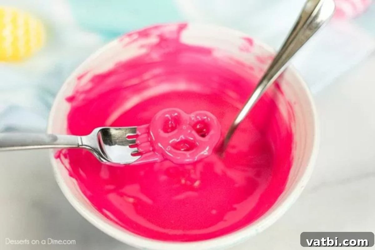 Melting pink candy melts in a bowl with a pretzel on a fork
