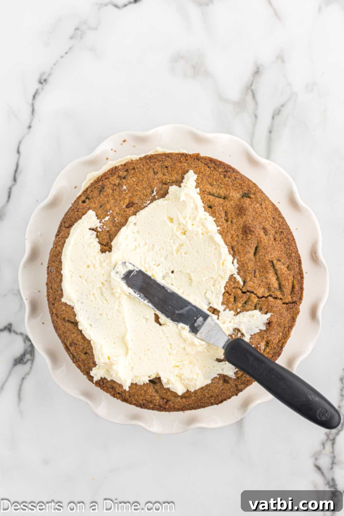 The first layer of Keto Carrot Cake on a plate, topped with a smooth, even layer of cream cheese frosting.