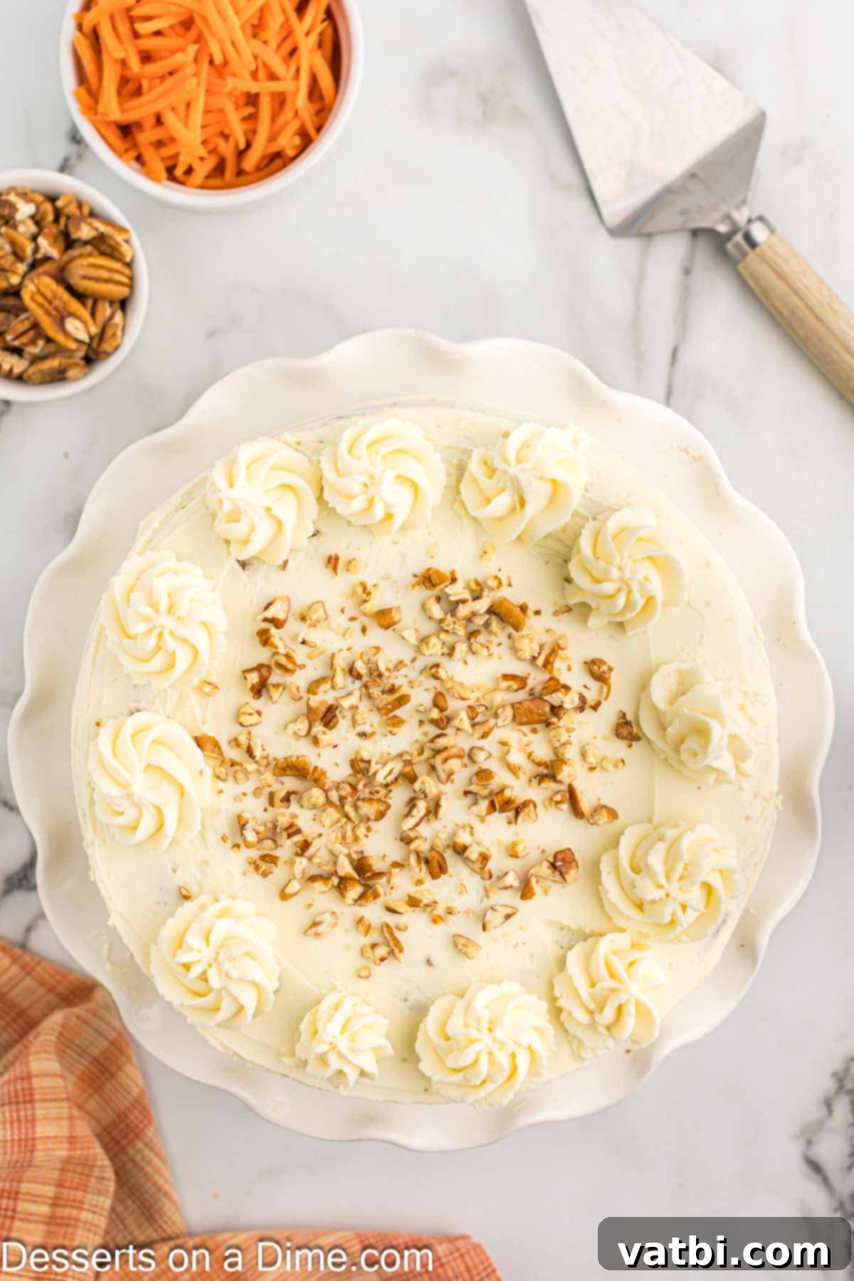 A wide shot of the fully assembled and decorated Keto Carrot Cake, topped with creamy frosting and scattered chopped pecans, looking absolutely mouthwatering.