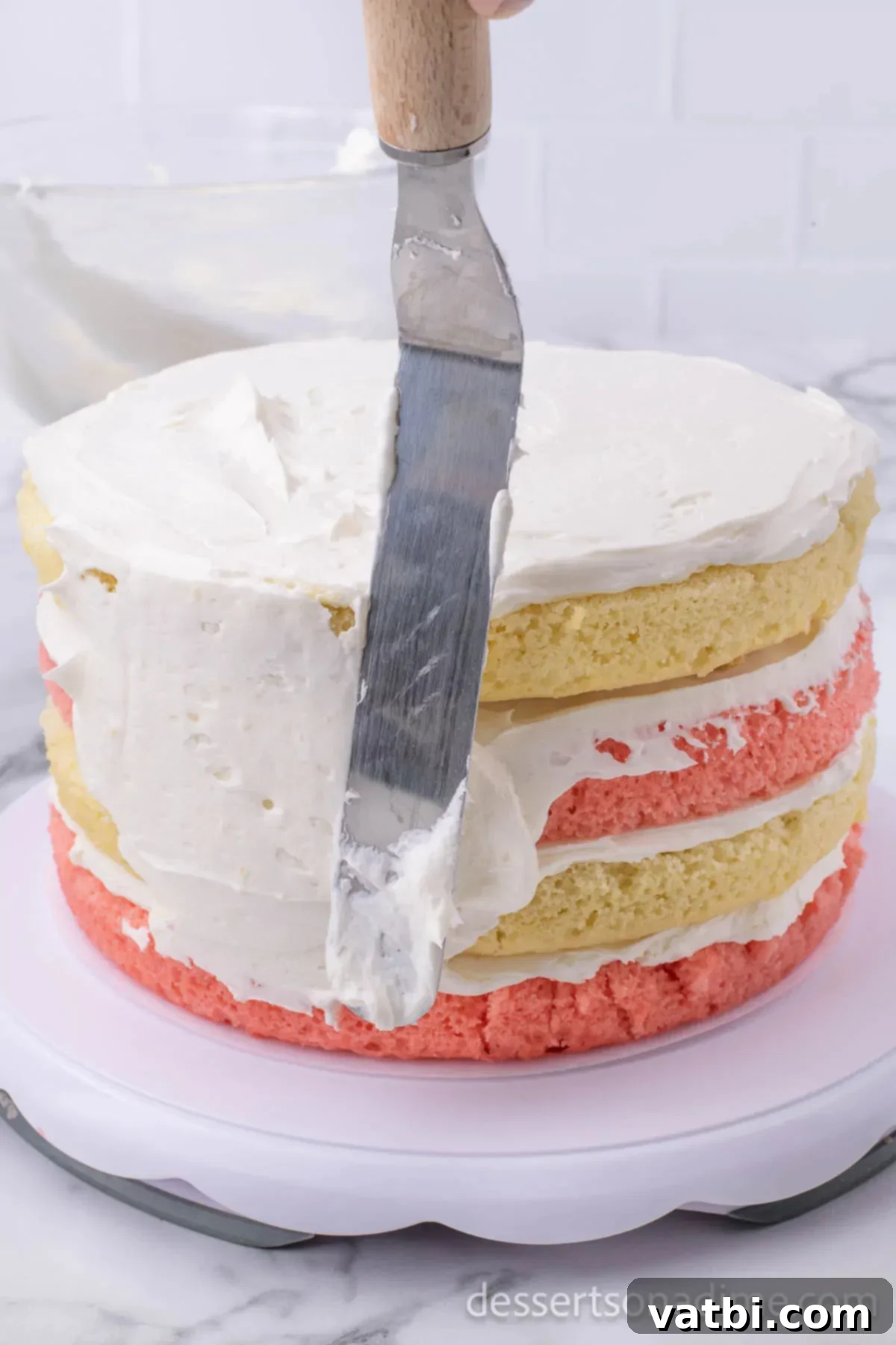 Heavenly Strawberry Crunch Cake 11 Frosting on side of cake with an offset spatula.