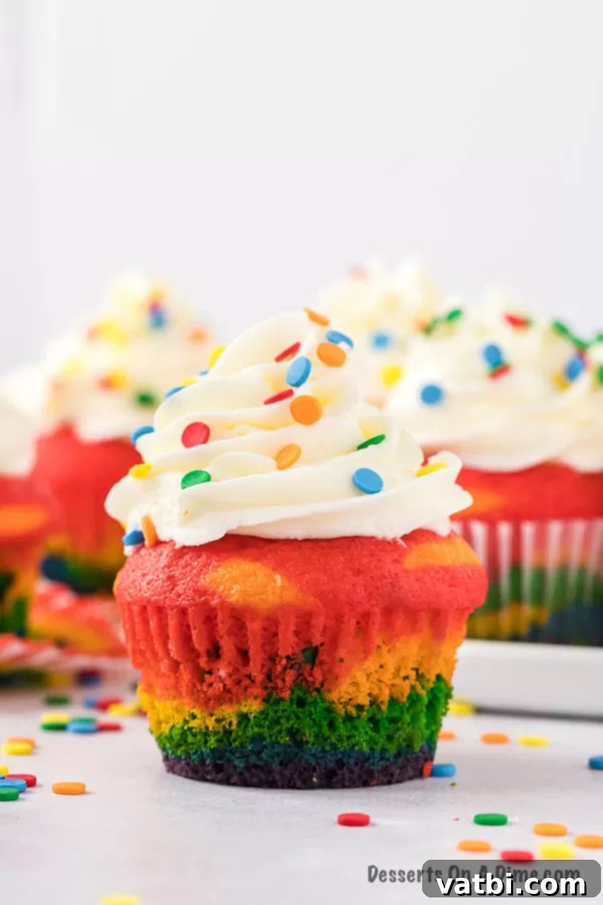 Spectrum Sweets 10 Close-up of rainbow cupcakes with fluffy white icing and sprinkles.