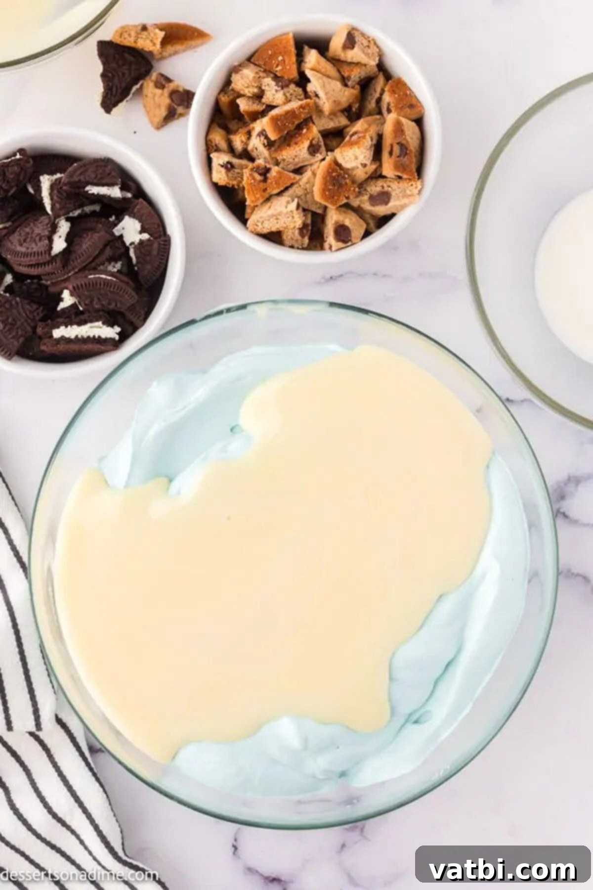 A large mixing bowl containing heavy cream, vanilla extract, and blue food coloring, ready to be whipped.