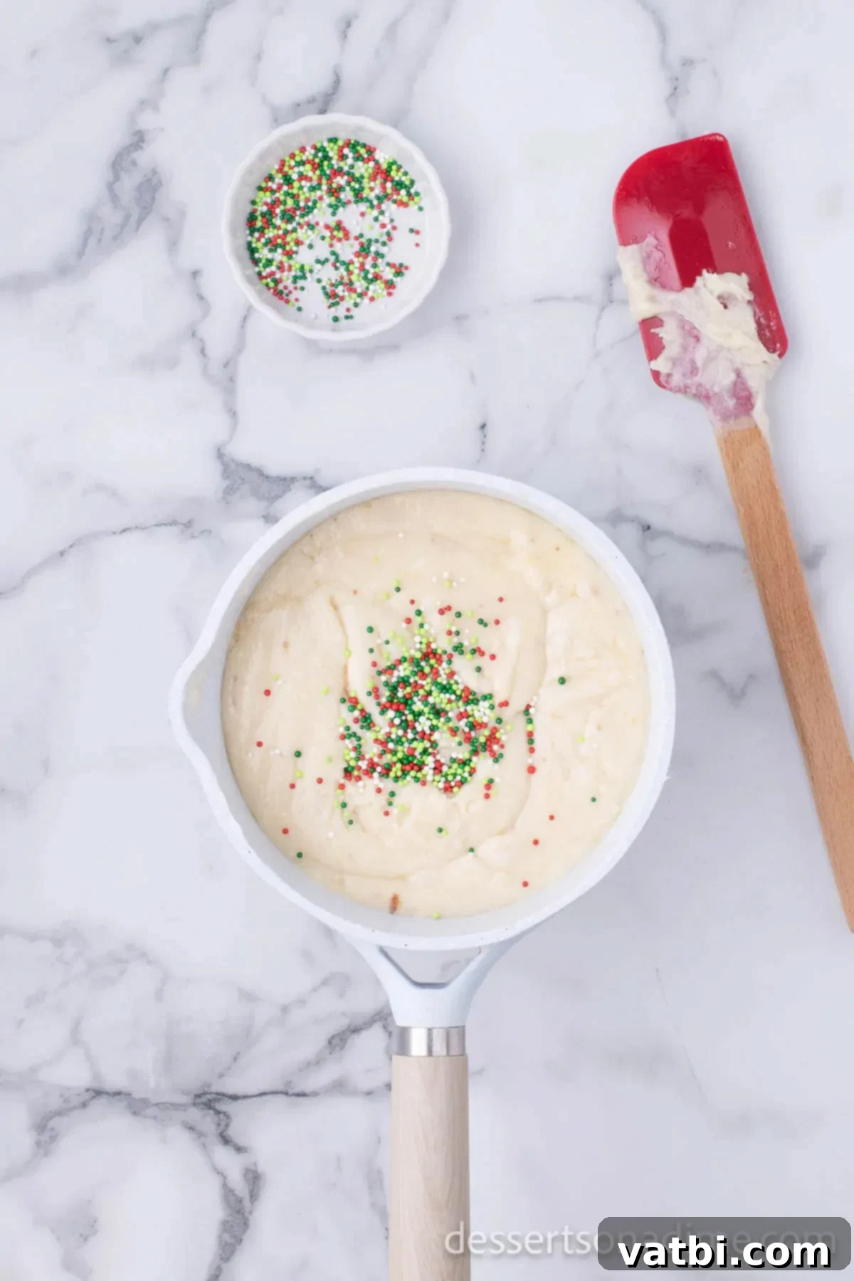 Ultimate Sugar Cookie Fudge 7 Half of the festive red, green, and white sprinkles being folded into the smooth sugar cookie fudge mixture in a saucepan.