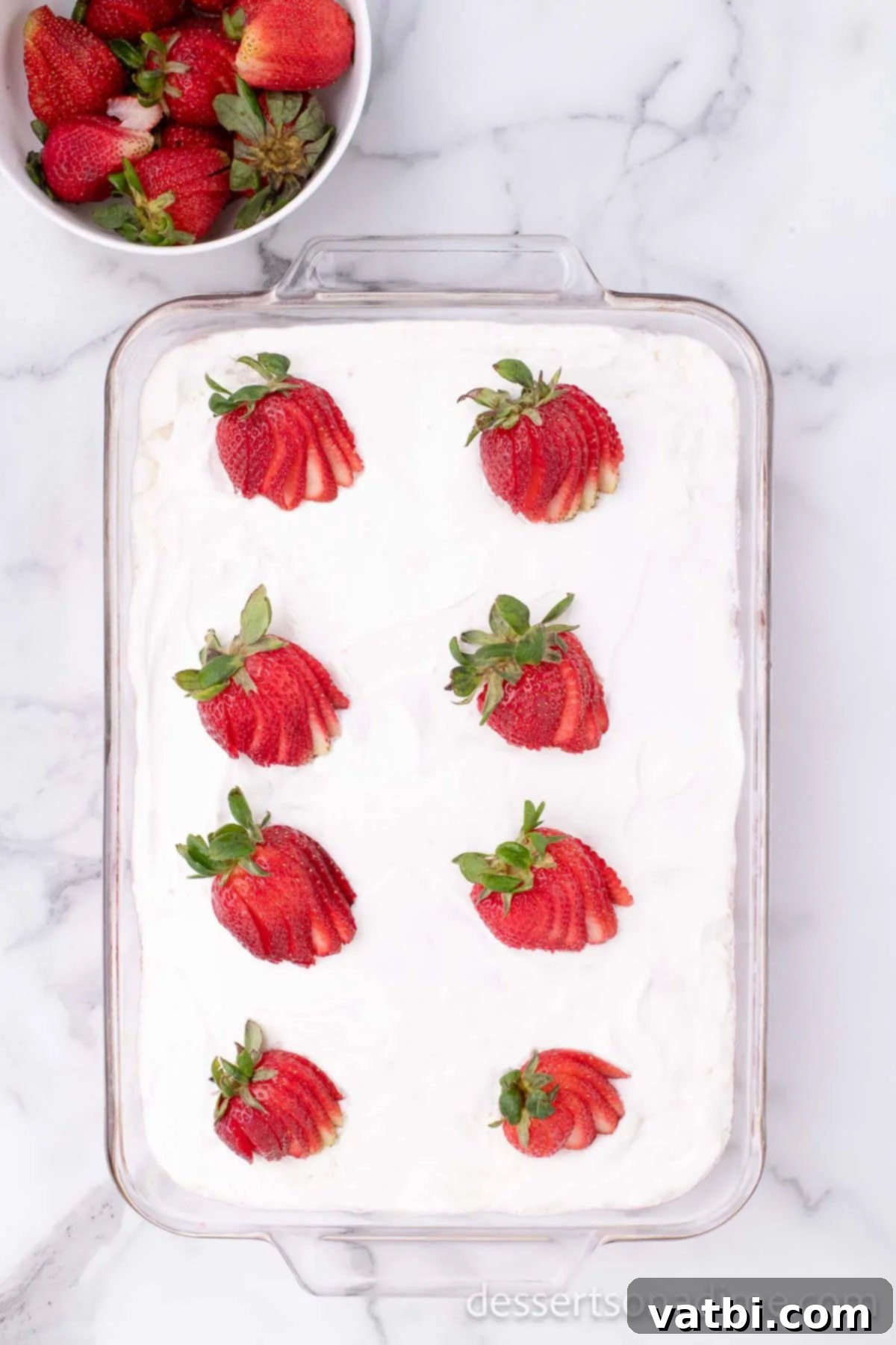 Strawberry Poke Cake topped with whipped topping and fresh strawberry slices.