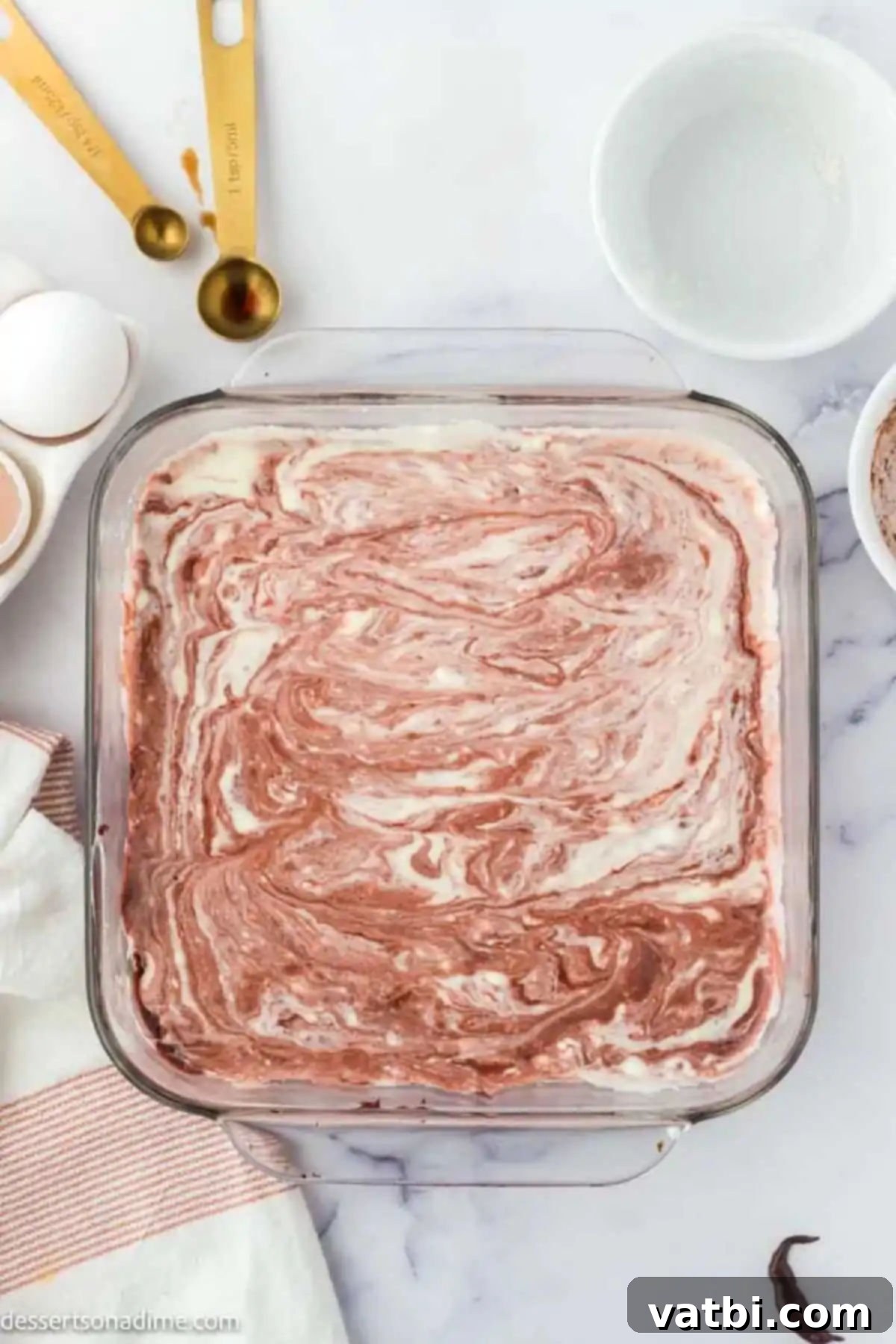 Cheesecake batter swirled into the red velvet brownie batter in a baking dish.