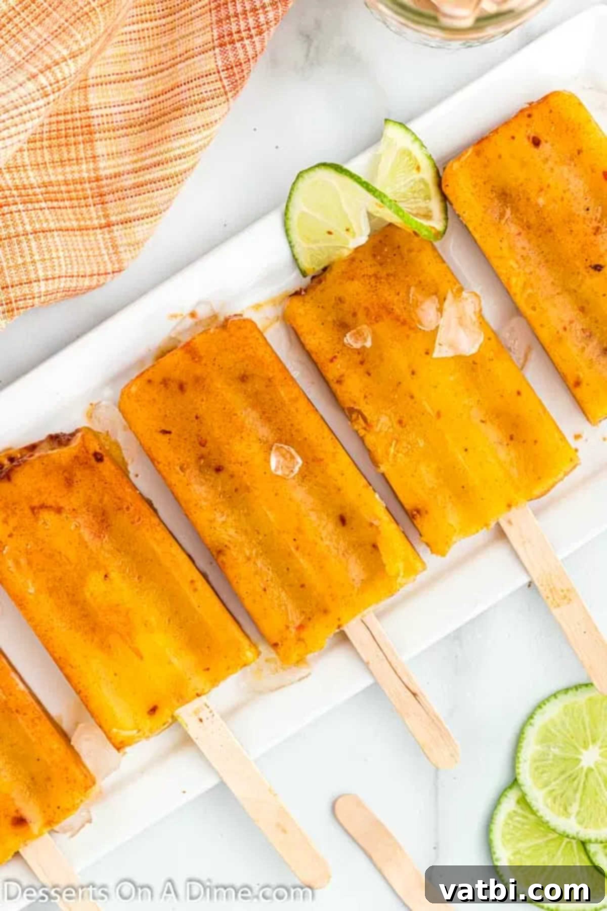Zesty Mango Tajin Popsicles 3 Another view of a mango tajin popsicle, glistening with frost, on a tray of ice.