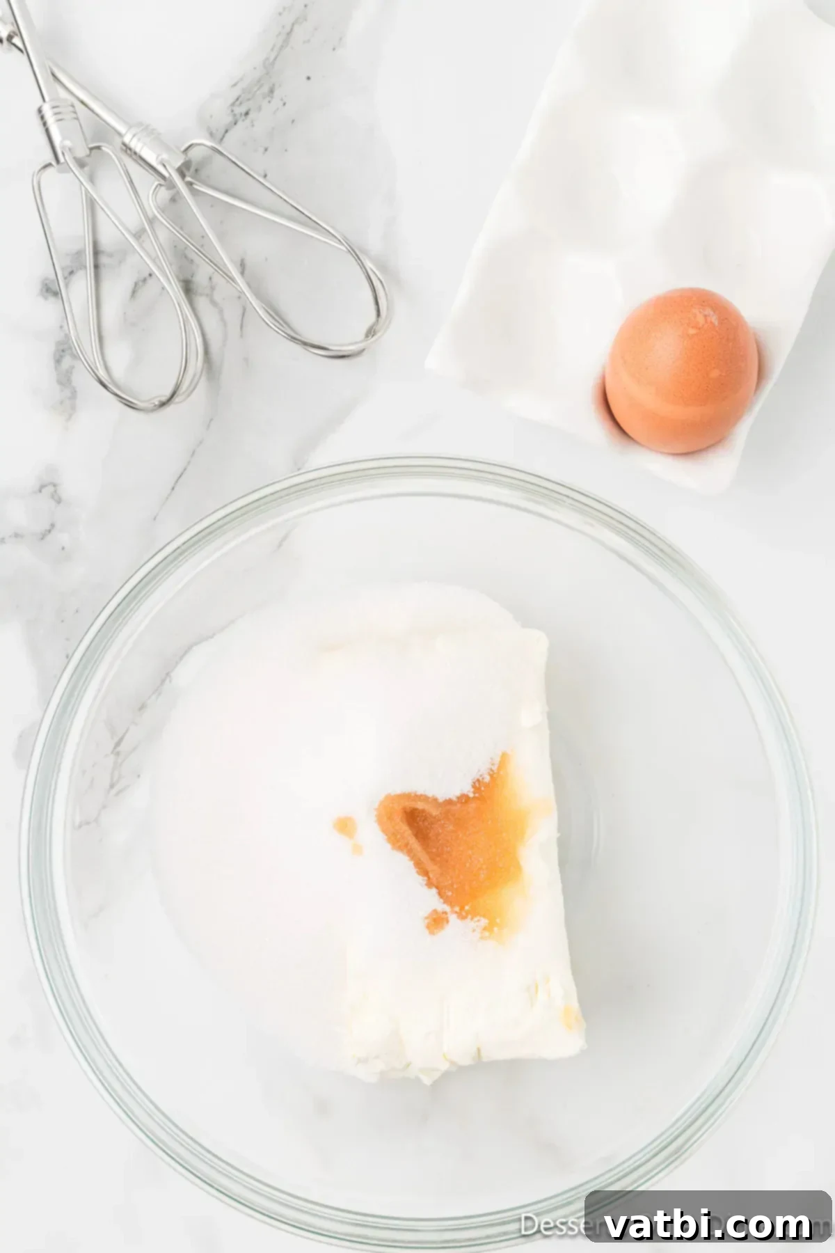 Dreamy Snickerdoodle Cheesecake Bars 4 Cream cheese, egg and vanilla combined in a bowl. A medium glass bowl contains softened cream cheese, a raw egg, and a measurement of vanilla extract, ready to be mixed.