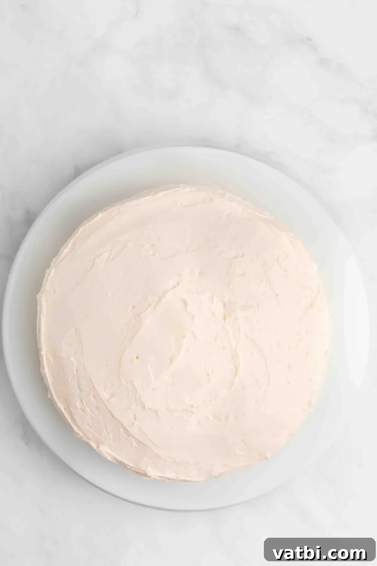 Perfect Cherry Chip Cake 12 Bottom cake layer on a platter being frosted with pink buttercream.
