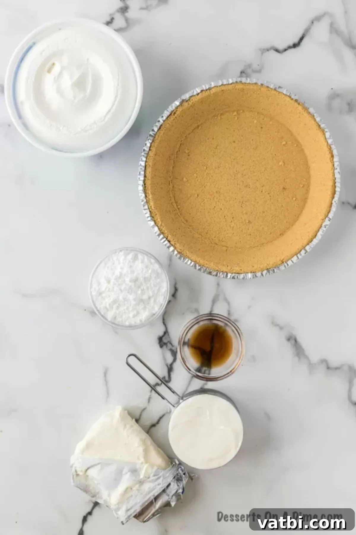 Effortless Philadelphia No-Bake Cheesecake 3 A flat lay photograph showcasing all the essential ingredients for a Philadelphia No-Bake Cheesecake: cream cheese, sour cream, powdered sugar, vanilla extract, a tub of Cool Whip, a prepared graham cracker crust, and a can of cherry pie filling.