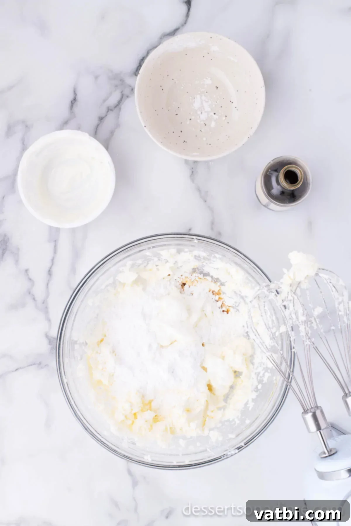 Effortless Philadelphia No-Bake Cheesecake 4 A large mixing bowl containing a creamy, light yellow mixture of cream cheese, sour cream, powdered sugar, and vanilla extract, being blended smoothly with a hand mixer.