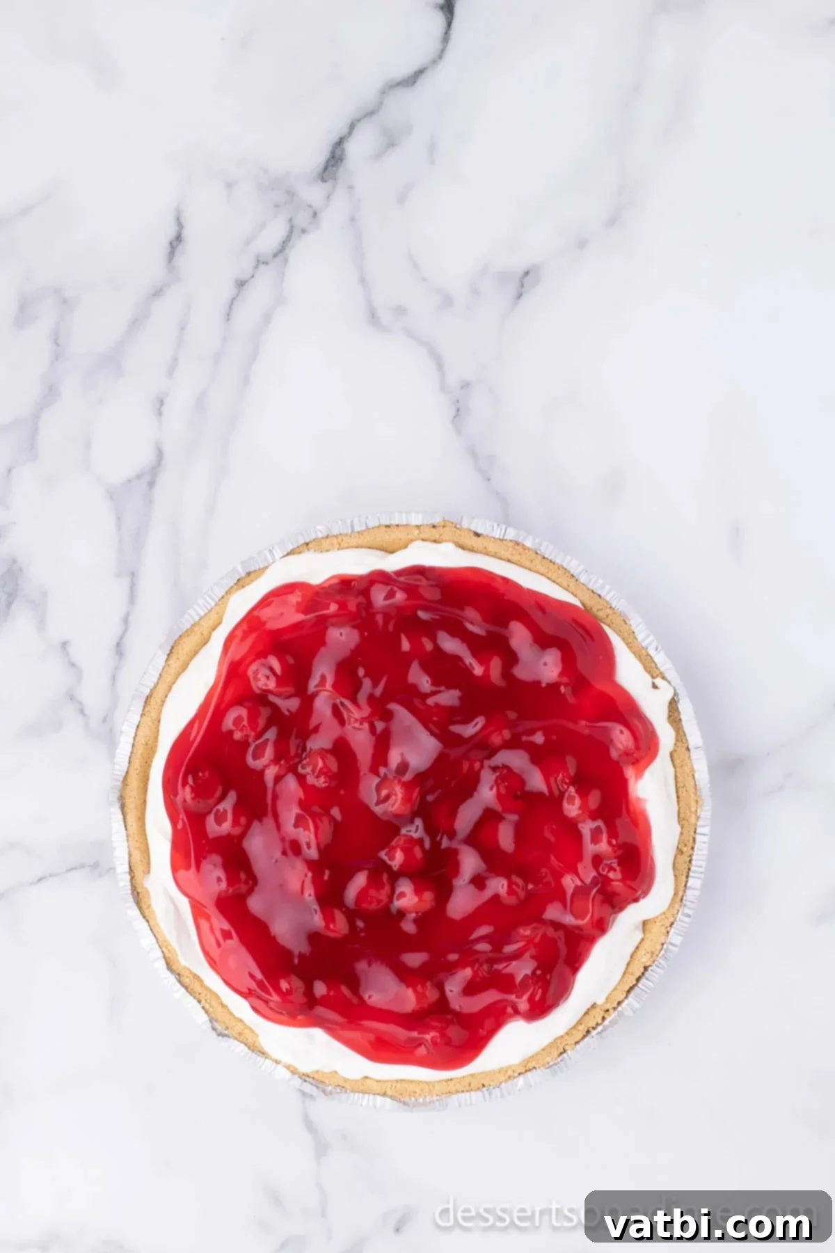 Effortless Philadelphia No-Bake Cheesecake 7 A completed no-bake cheesecake, freshly chilled, with a glossy layer of bright red cherry pie filling spread across its top, ready to be served.