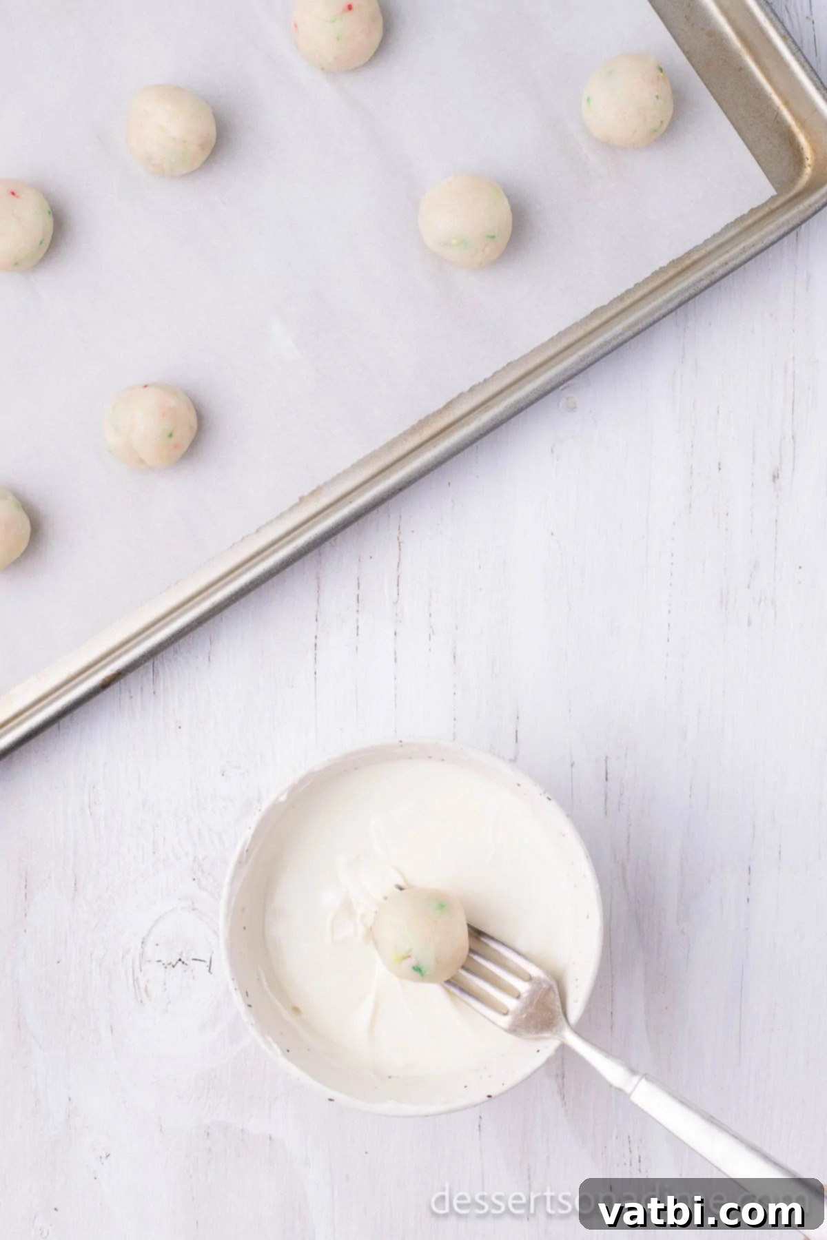 Holiday Truffle Magic 8 Chilled Christmas truffle balls being dipped into melted white chocolate using a fork.