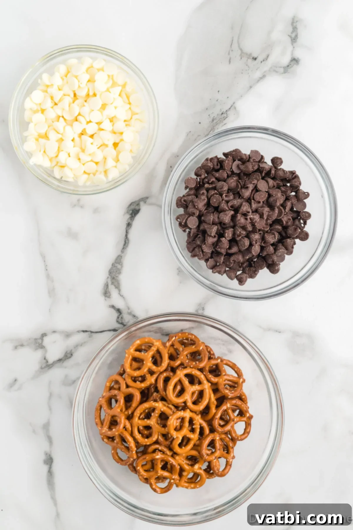 Sweet & Salty Pretzel Bliss 3 Two bowls, one with white chocolate chips and one with semi-sweet chocolate chips, alongside a bag of miniature pretzel twists, laid out as ingredients for chocolate covered pretzels.