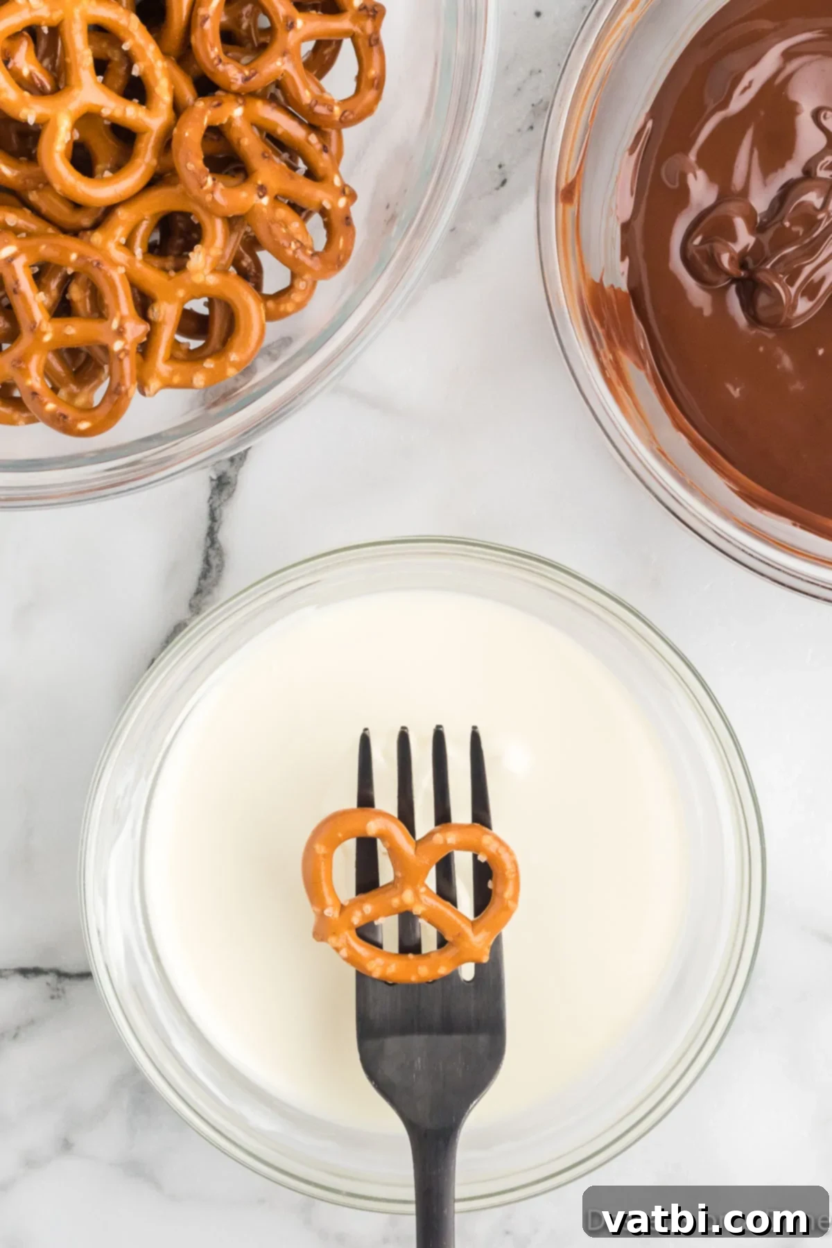 Sweet & Salty Pretzel Bliss 7 A pretzel held by a fork, ready to be dipped into a bowl of melted white chocolate.