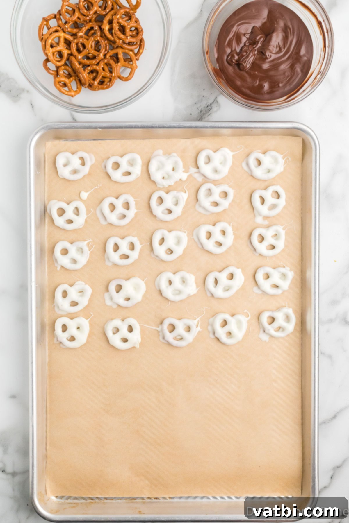 Sweet & Salty Pretzel Bliss 8 Several white chocolate-covered pretzels neatly arranged on a baking sheet lined with parchment paper, awaiting further decoration or setting.