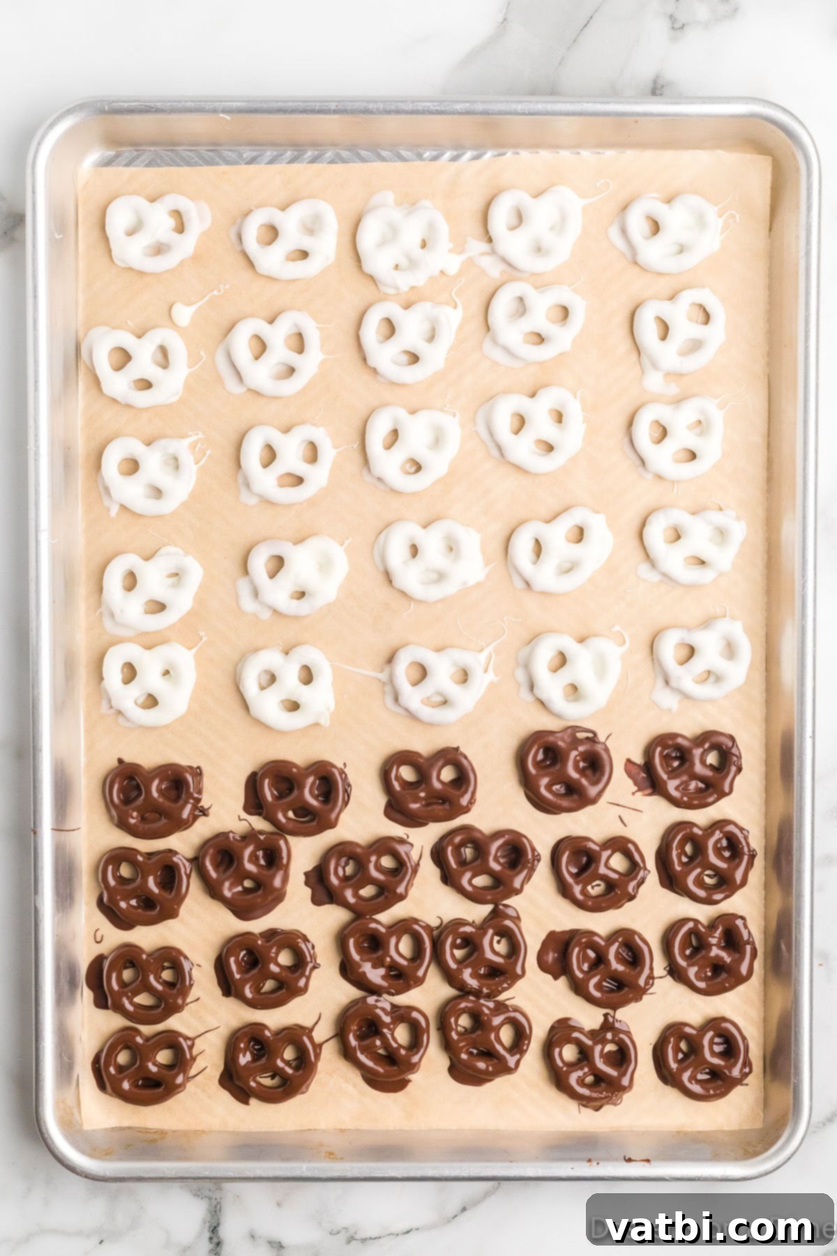Sweet & Salty Pretzel Bliss 9 A baking sheet filled with an assortment of white and milk chocolate-covered pretzels, some already drizzled, showcasing the variety in decoration.