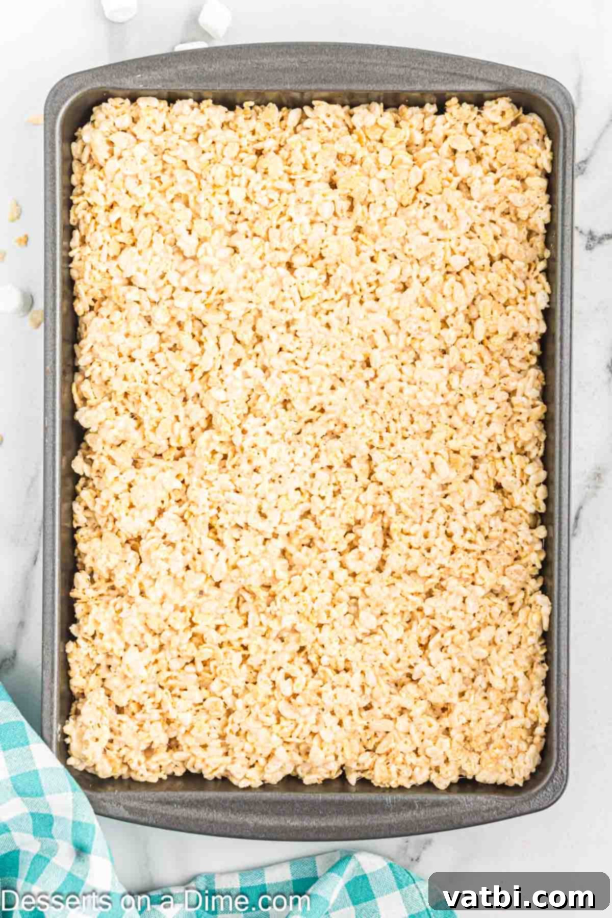 The Ultimate Rice Krispie Treat Recipe 9 Rice Krispie Treat mixture being pressed into a prepared baking pan.