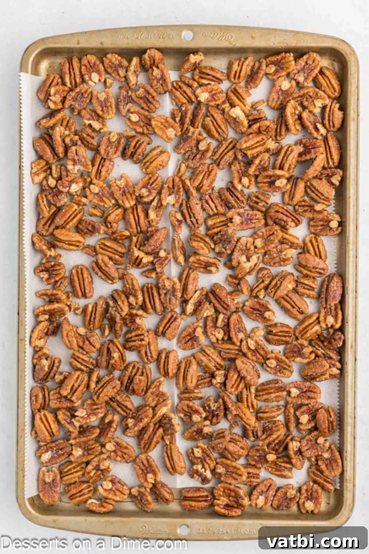 Coated candied pecans spread out in a single layer on a baking sheet lined with parchment paper.