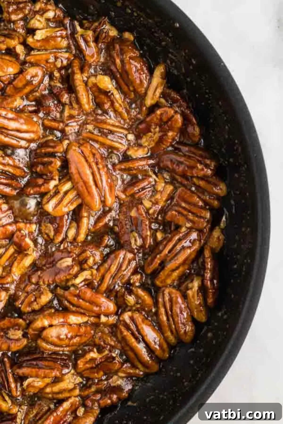 Freshly made candied pecans cooling in a skillet, still glistening with their sweet coating.