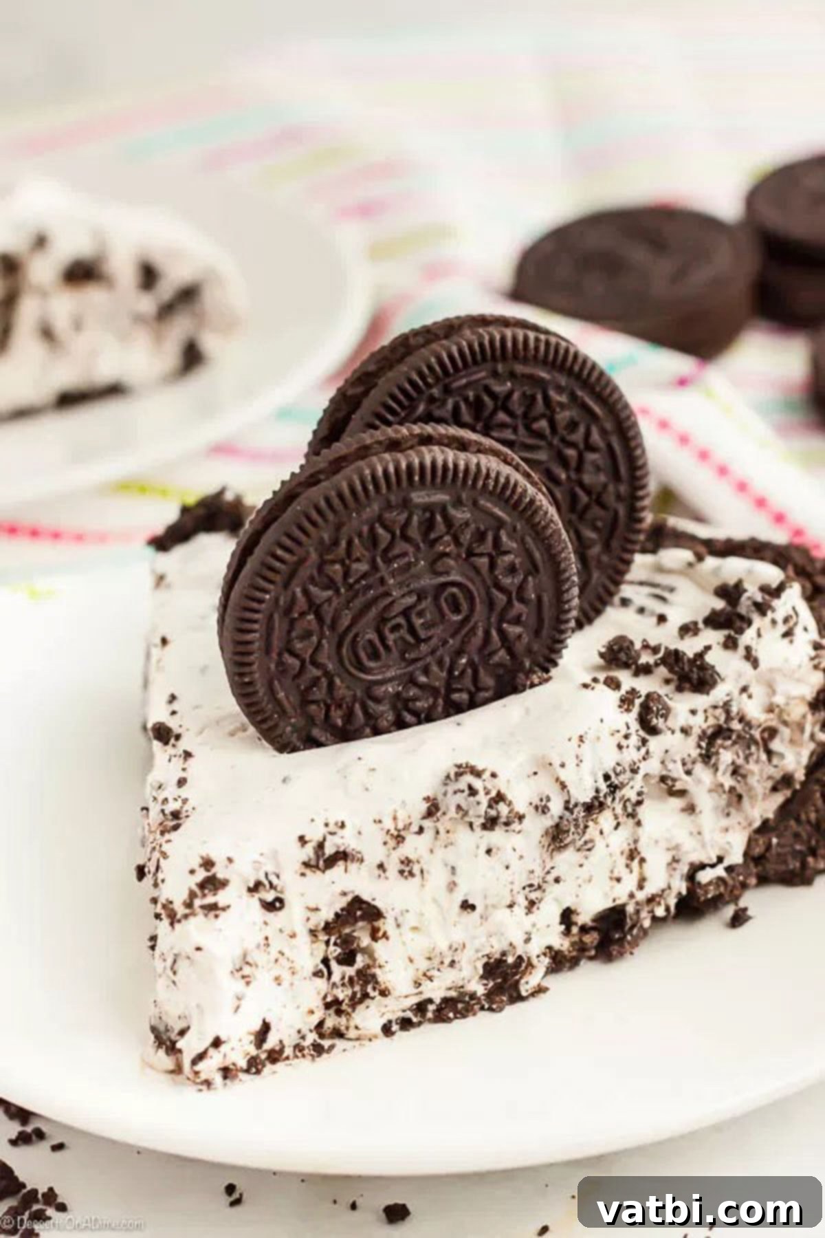 No Bake Oreo Pie Recipe is one of our favorite no bake treats. Everyone loves Oreo cookies so a pie seemed like a great idea! It is so creamy and delicious. A beautifully presented slice of No-Bake Oreo Pie on a white plate, garnished with whole Oreo cookies. Another slice is visible in the background.