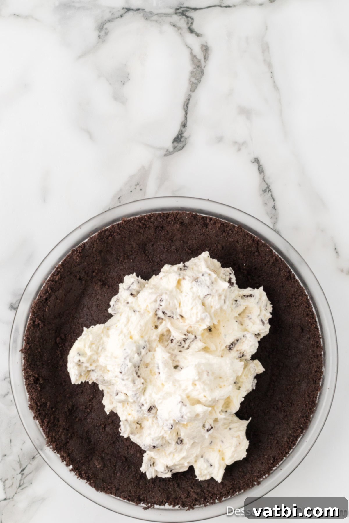 Effortless Oreo Indulgence 8 Cream cheese and Oreo filling being spooned into the chilled Oreo pie crust.