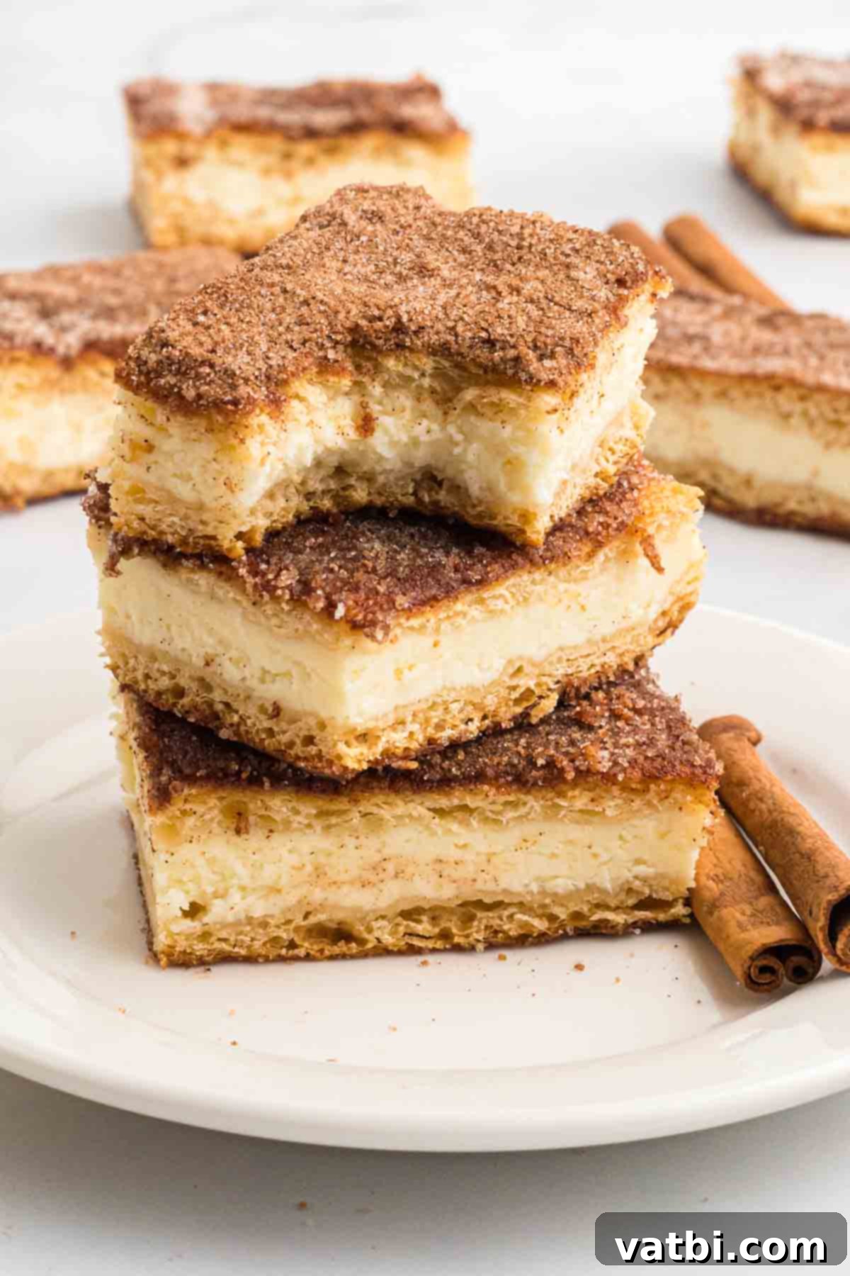 Cinnamon Sugar Cheesecake 14 A beautifully arranged stack of golden-brown churro cheesecake bars, dusted with cinnamon sugar, on a white plate, ready to be enjoyed.