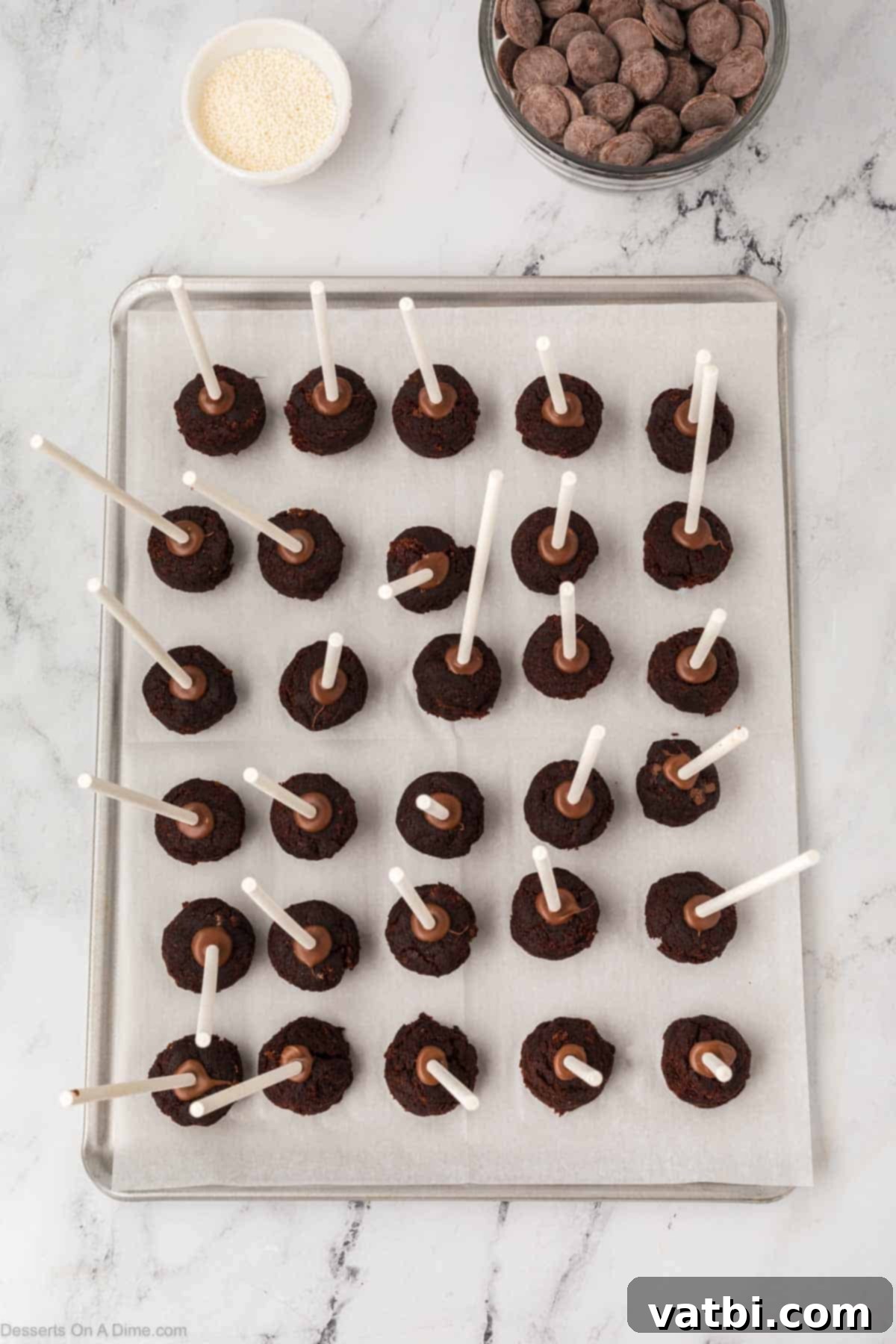 Copycat Starbucks Chocolate Cake Pops 12 Chocolate cake balls with lollipop sticks inserted halfway, arranged on a baking sheet, ready for freezing.