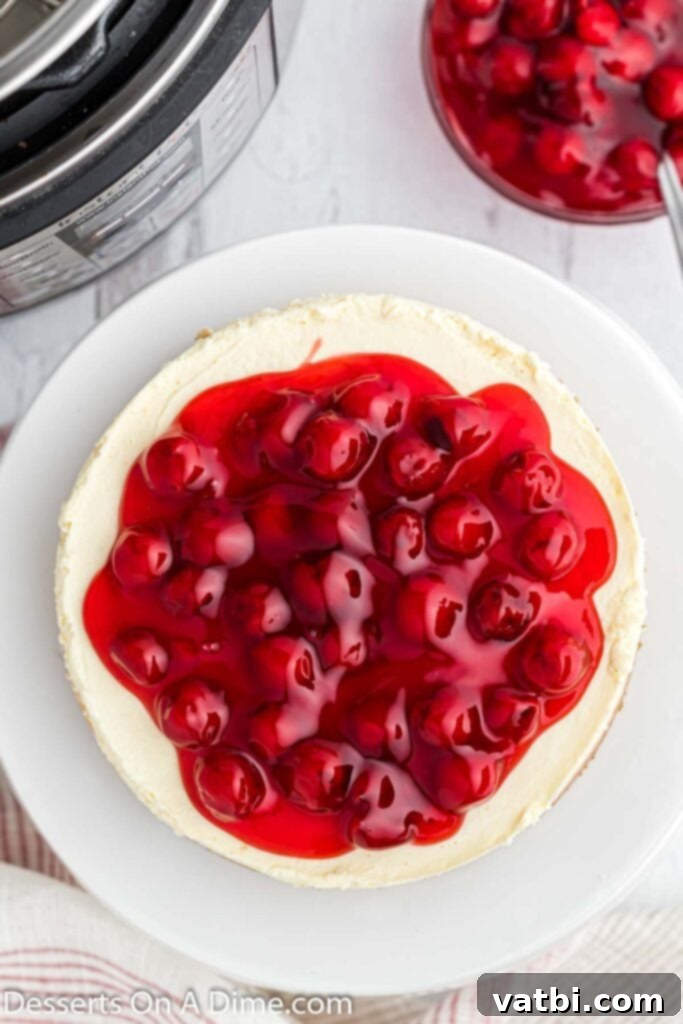 Instant Pot Cheesecake Perfection 9 A slice of Instant Pot cheesecake on a plate, topped with cherry pie filling and a fork beside it.
