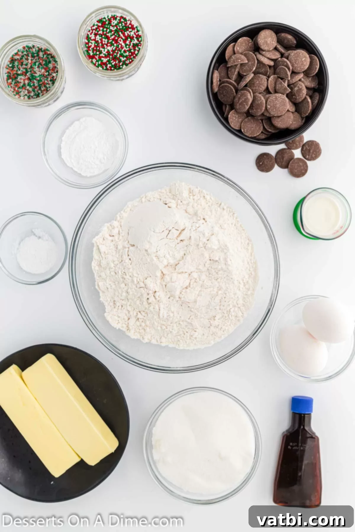 Irresistible Chocolate Dipped Sugar Cookies 3 A neatly arranged display of ingredients for Chocolate dipped sugar cookies, including butter, eggs, vanilla, milk, all-purpose flour, baking powder, salt, granulated sugar, chocolate melting wafers, and festive sprinkles.
