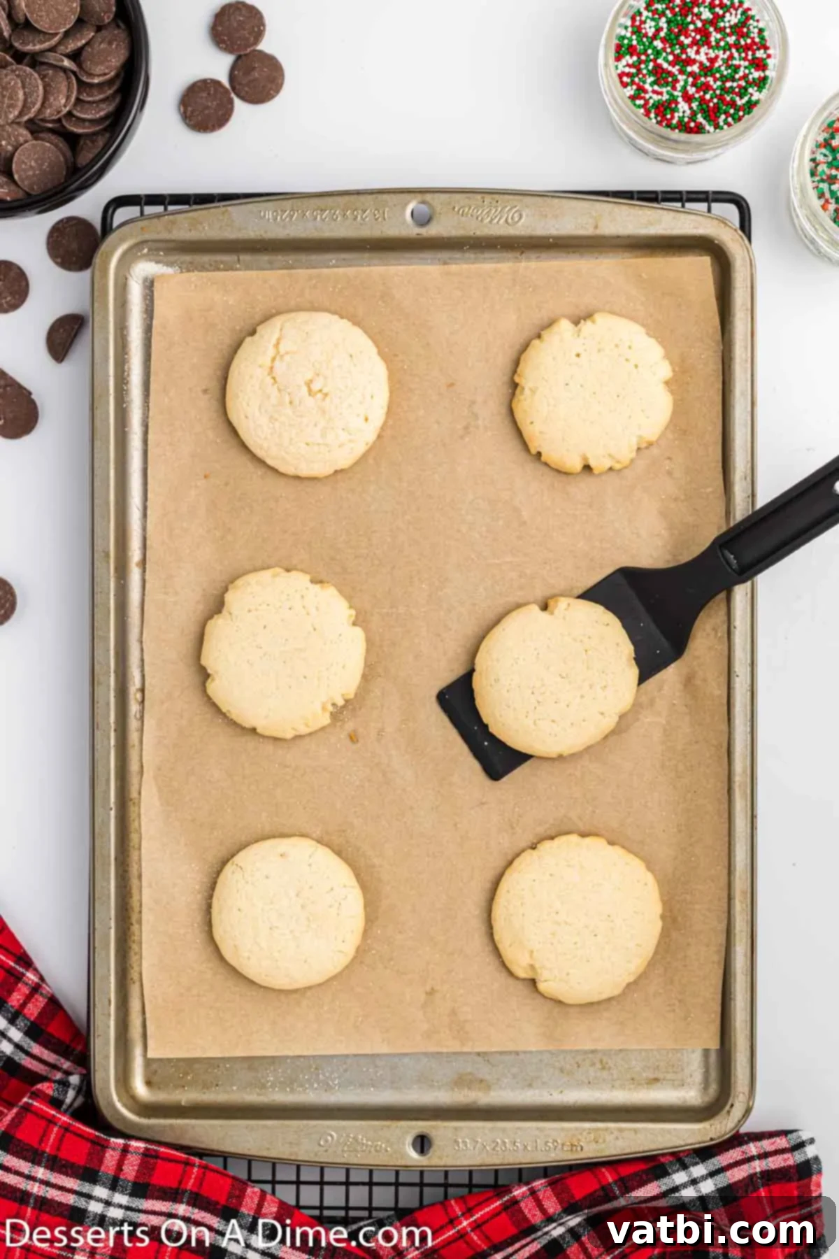 Irresistible Chocolate Dipped Sugar Cookies 7 Freshly baked sugar cookies being transferred from a baking sheet to a wire cooling rack.
