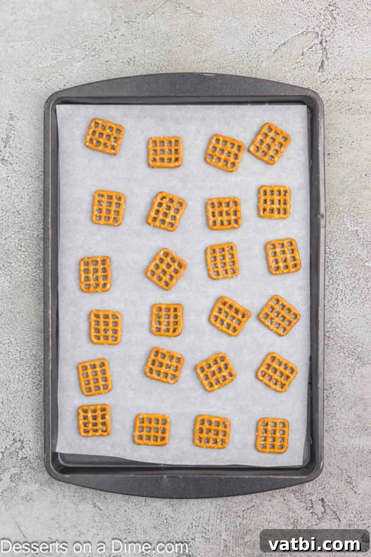 Snaps pretzels laid out neatly in a single layer on a baking sheet lined with parchment paper, preparing for toppings.
