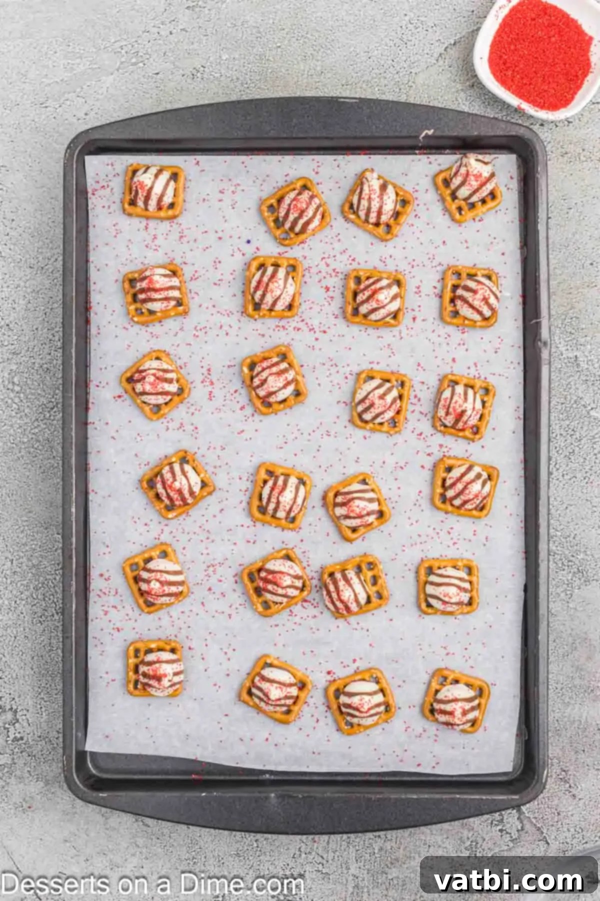 Red sanding sugar sprinkled immediately and evenly over the warm, melted Hershey Hugs on pretzels, creating a bloodshot effect.