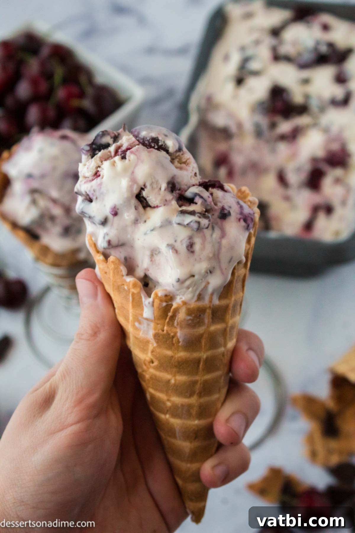 Homemade Cherry Garcia Ice Cream 2 A scoop of homemade Cherry Garcia ice cream in a waffle cone, garnished with fresh cherries.