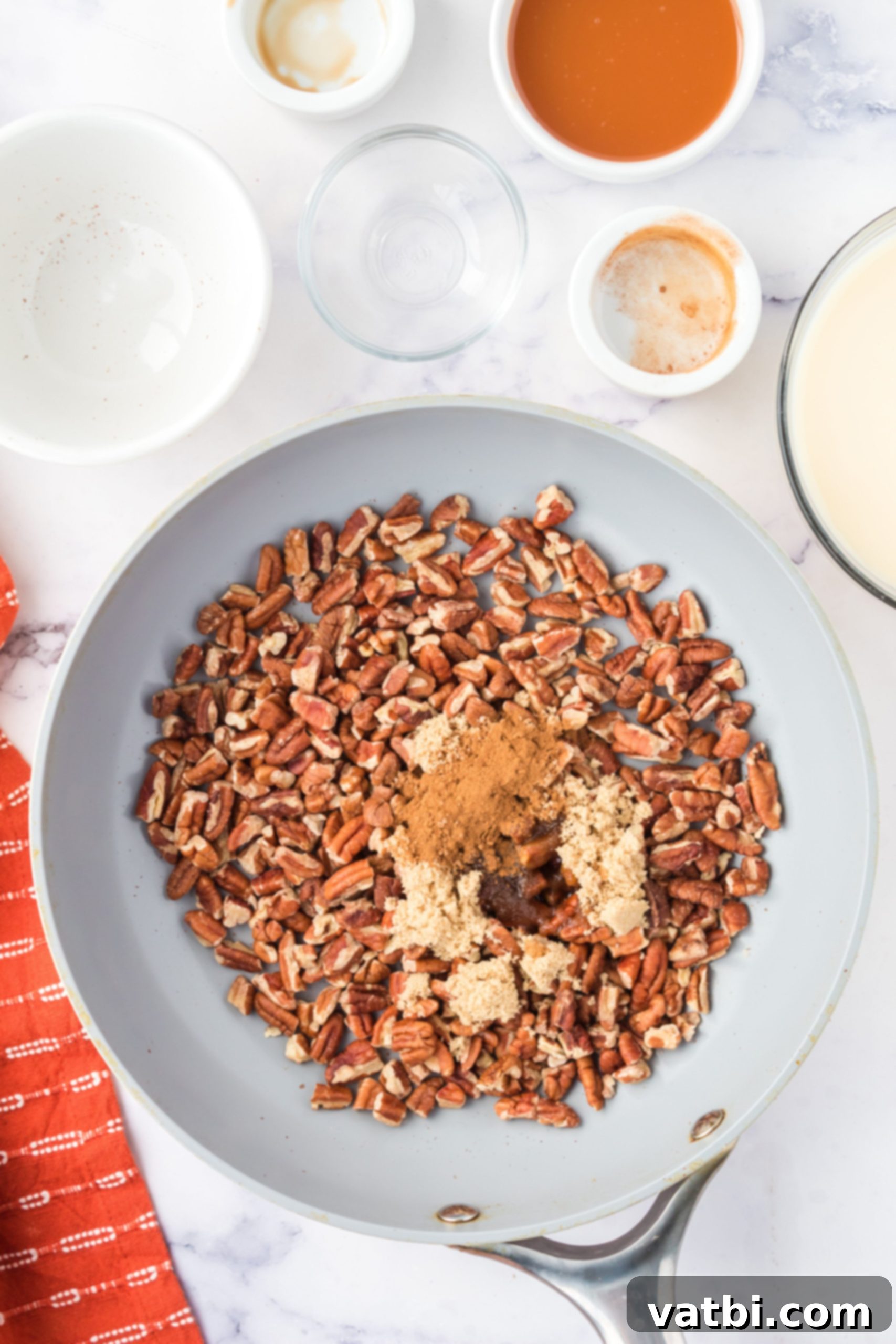 Pecans in a pan with brown sugar, salt, cinnamon, and vanilla.