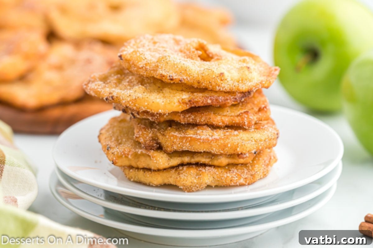 Golden Apple Fritters 2 Deep fried apples stacked together on a white plate, glistening with cinnamon sugar.