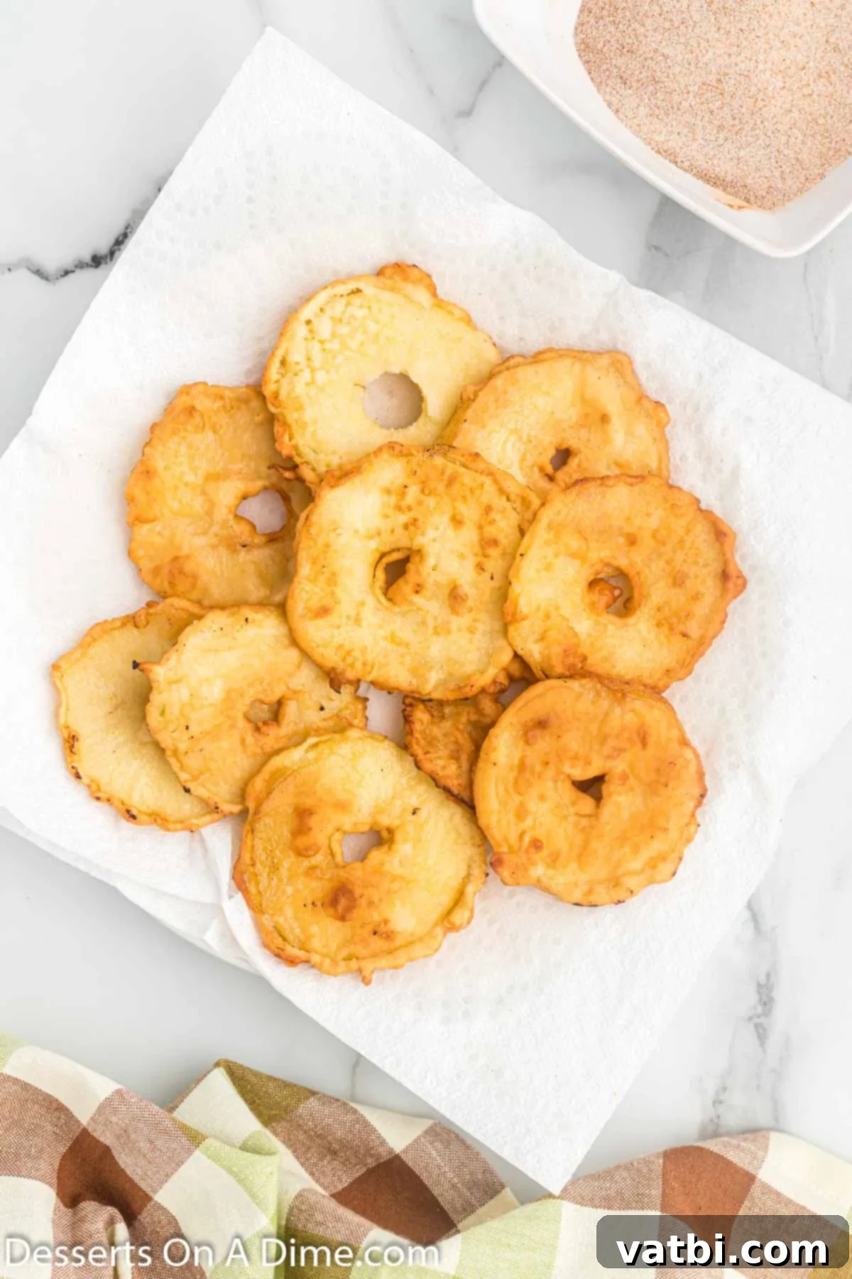 Golden Apple Fritters 6 Fried apples cooling on a plate lined with paper towels.